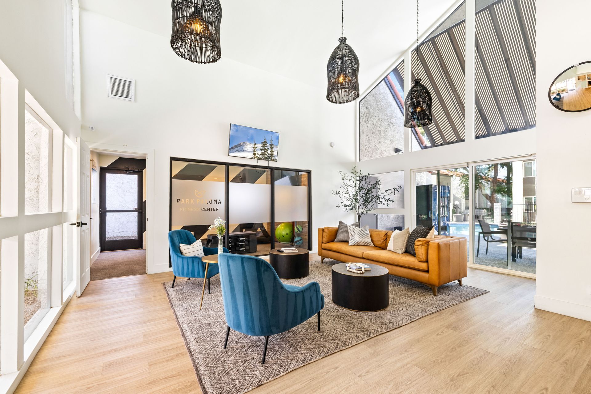 Bright living room with blue chairs, tan sofa, and decorative hanging lights. Large windows and glass doors.