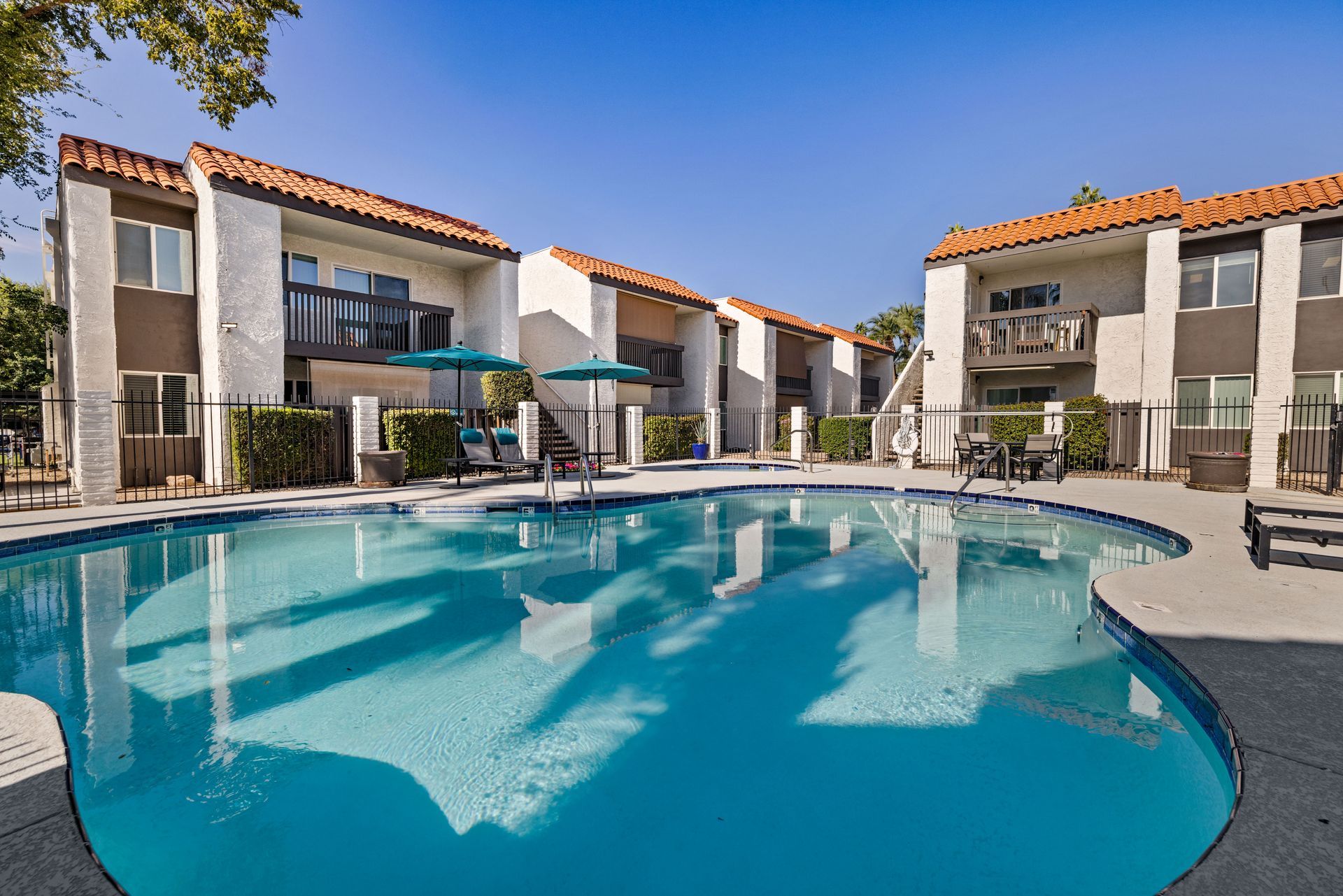 Apartment complex with a pool; buildings with white walls and red tile roofs, blue pool.