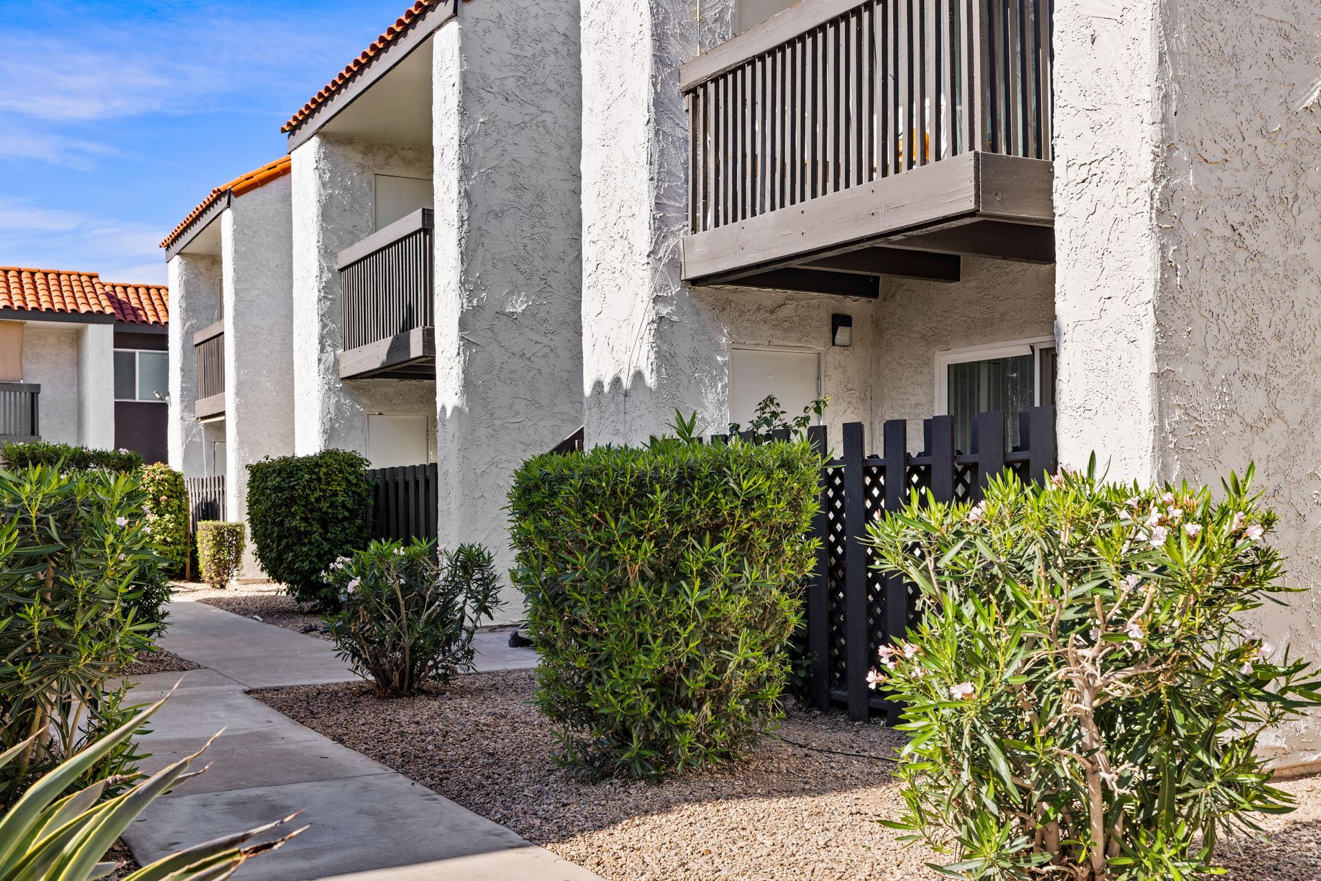 Apartment building exterior, stucco walls, brown balconies, green bushes, blue sky.