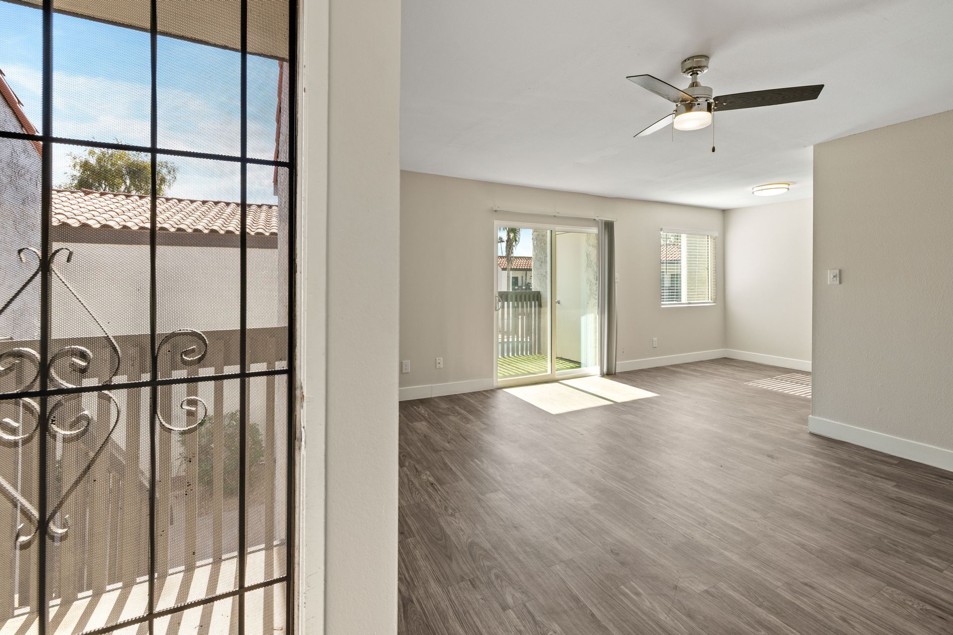 Empty living room with wood-look flooring, ceiling fan, and sliding glass door leading to a yard.
