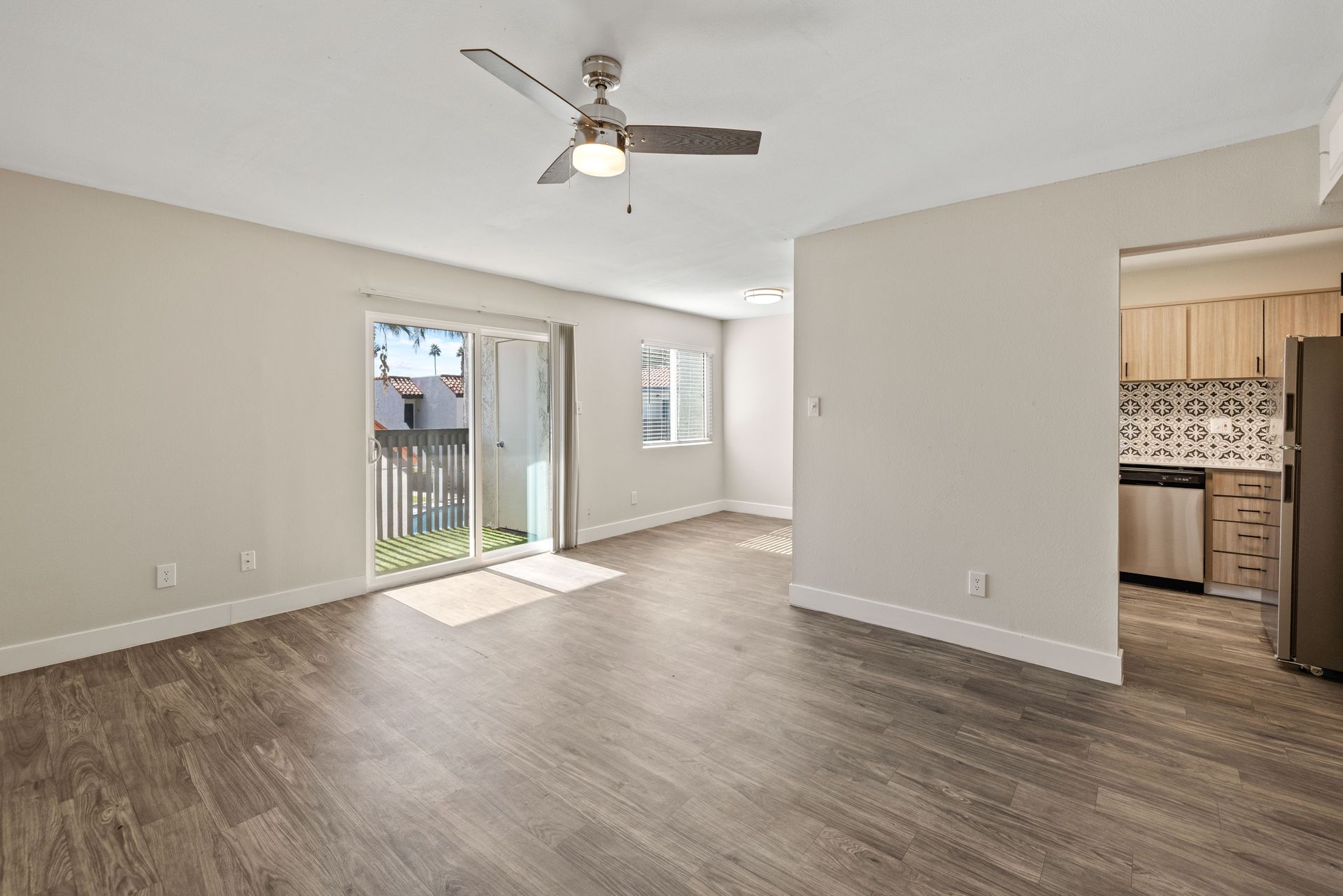 Empty living room with wood-look flooring, sliding door to a patio, and a doorway to a kitchen.