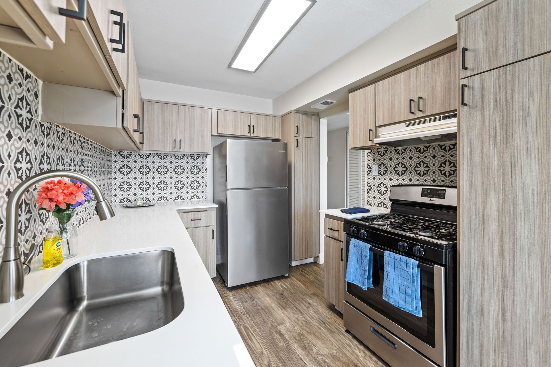 Modern kitchen with light wood cabinets, stainless steel appliances, and patterned backsplash.