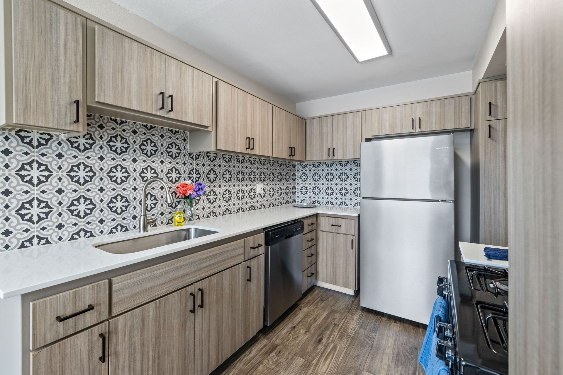 Kitchen with light wood cabinets, patterned backsplash, stainless steel appliances, and white countertop.