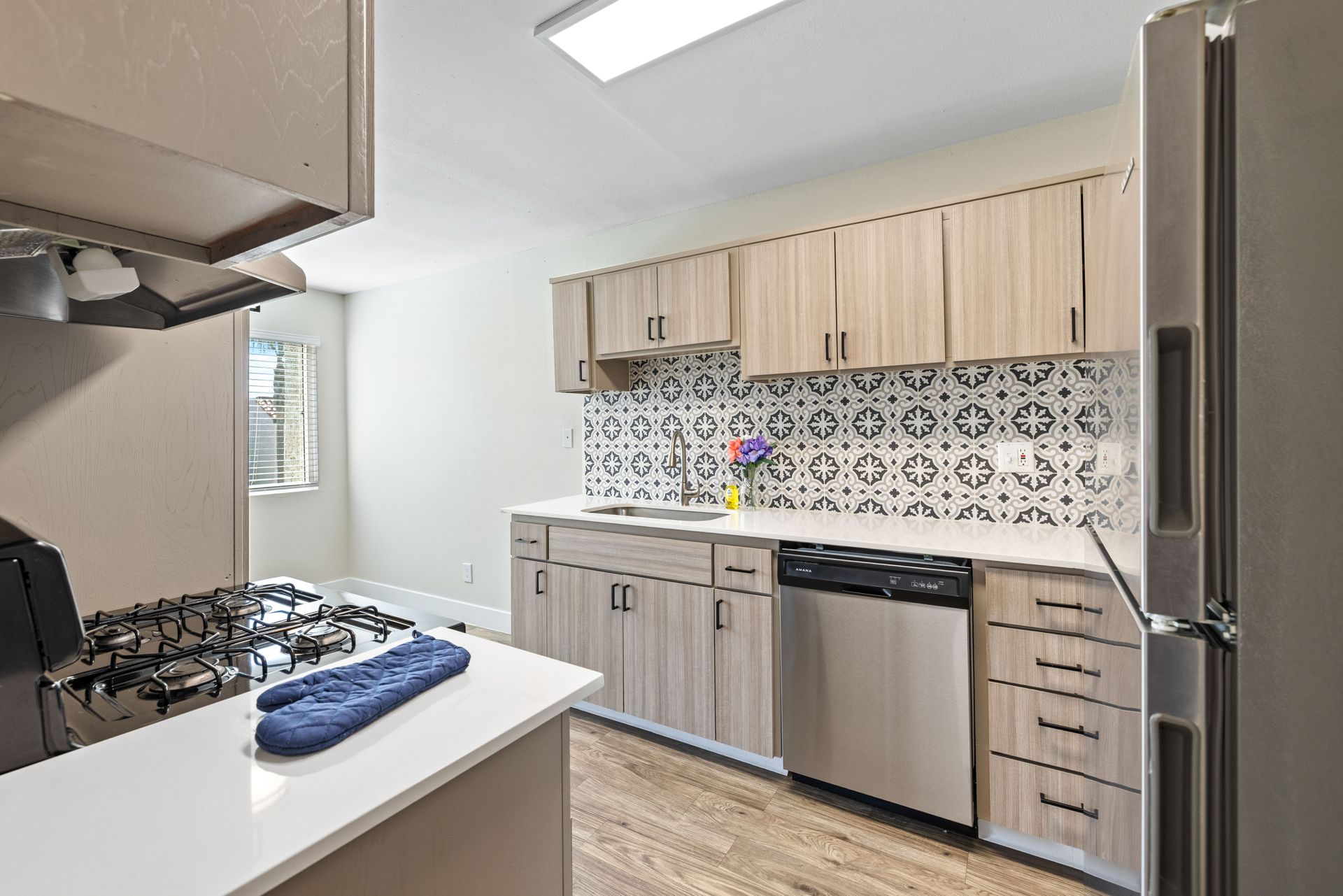 Kitchen with light wood cabinets, patterned backsplash, stainless steel appliances, and a window.