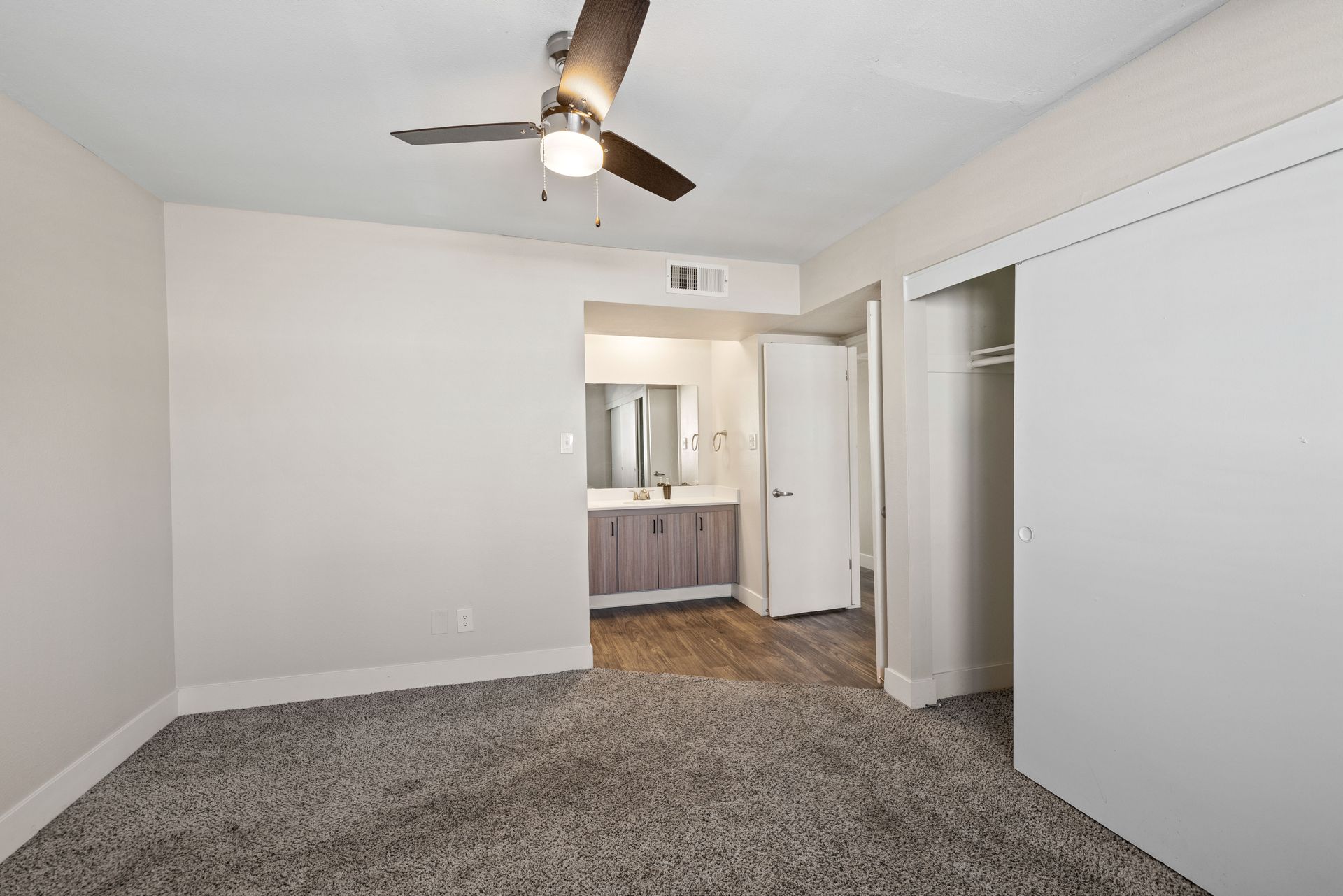 Bedroom with carpet, closet, ceiling fan, and access to a bathroom with a vanity and mirror.