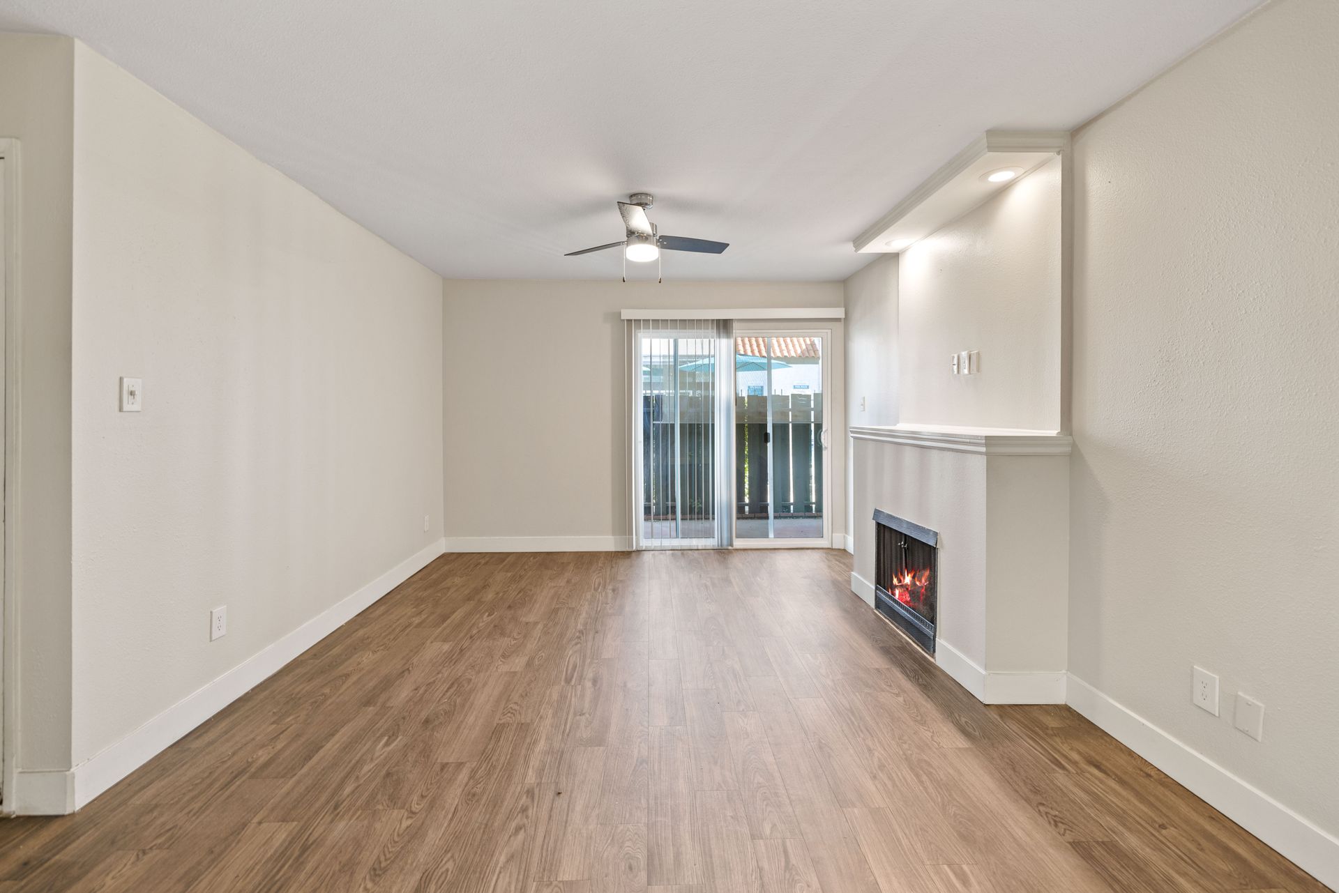 Empty living room with fireplace, sliding glass door to balcony, and wood-look flooring.