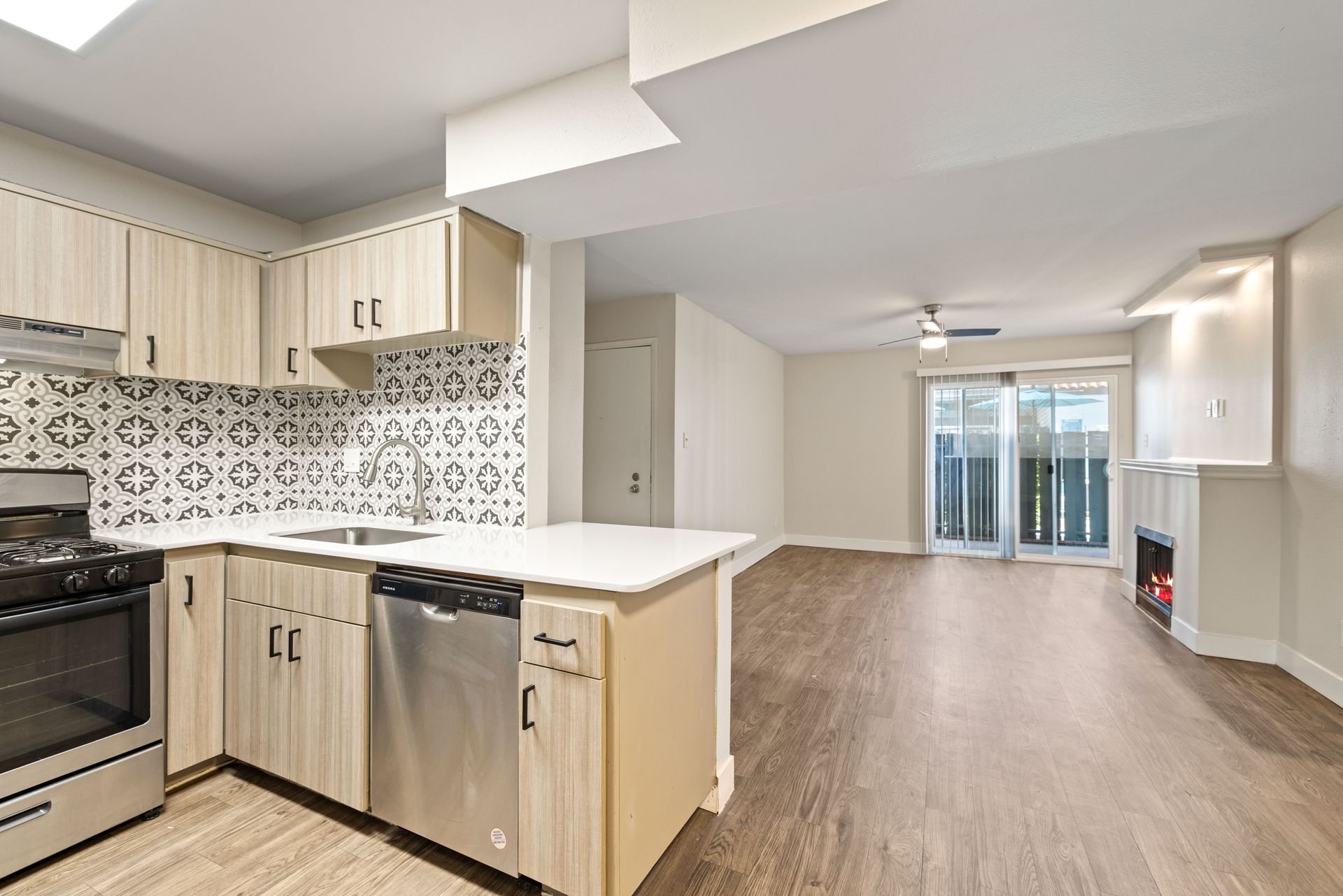 Kitchen and living area combo with wood cabinets, patterned backsplash, and fireplace.