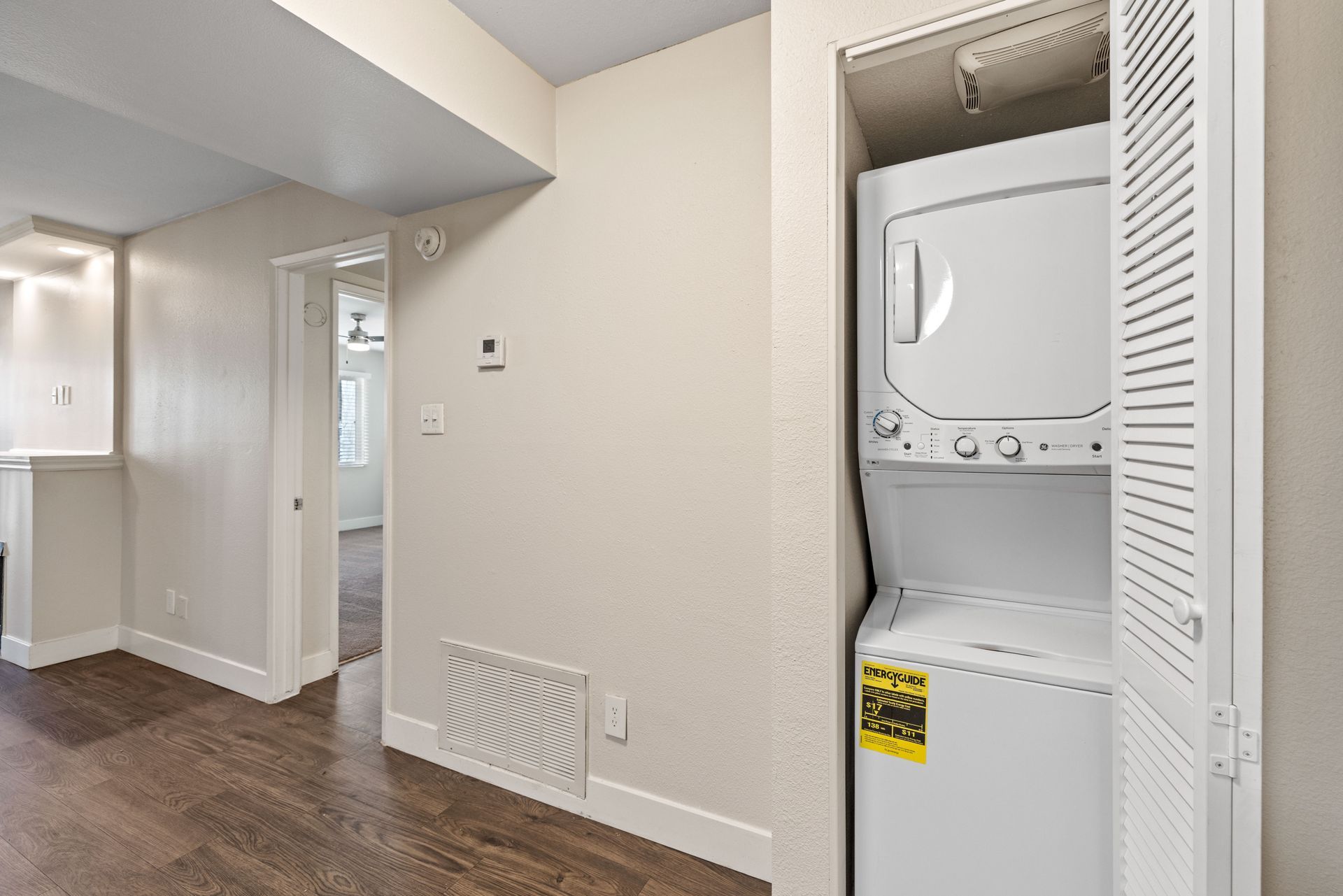 Interior view with stacked washer and dryer in a closet; hallway with wood flooring.