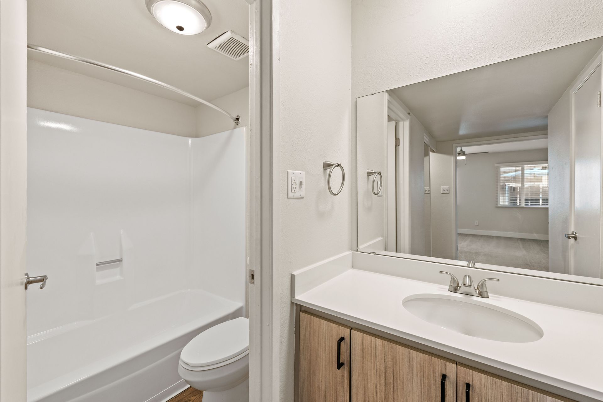 Bathroom with white tub/shower, toilet, vanity with sink, and large mirror.
