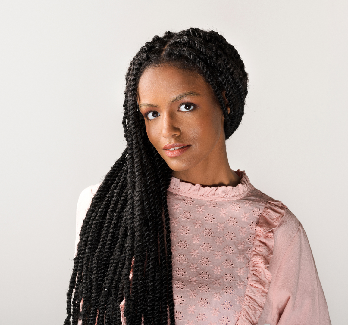 A woman with braids is wearing a pink shirt and looking at the camera.