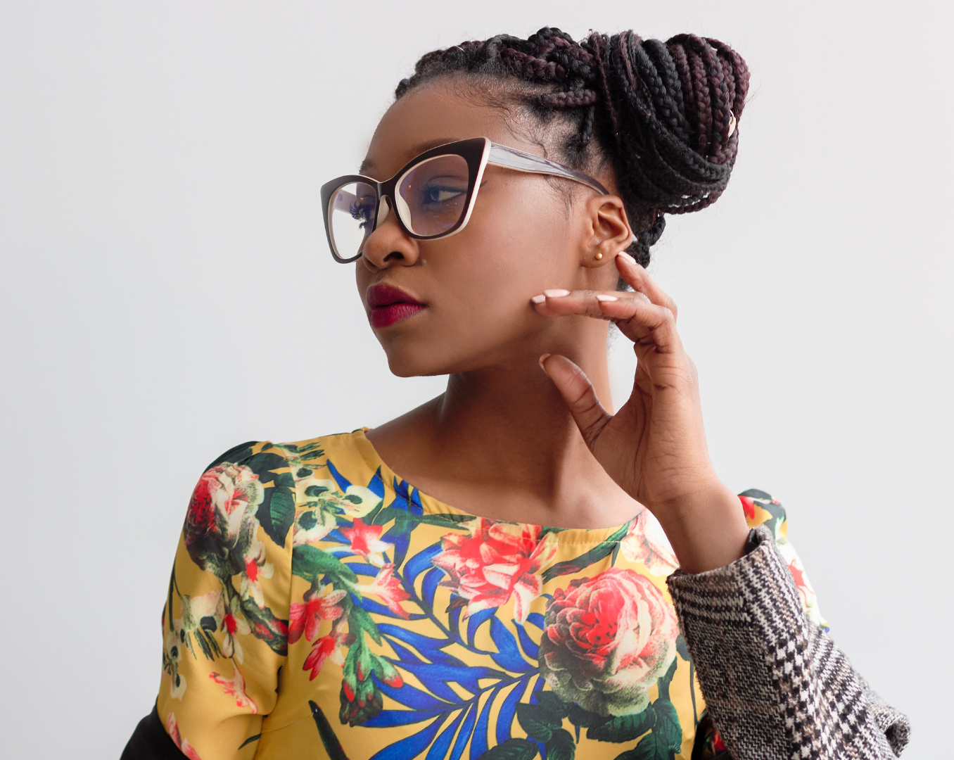 A woman wearing glasses and a floral shirt is touching her face.
