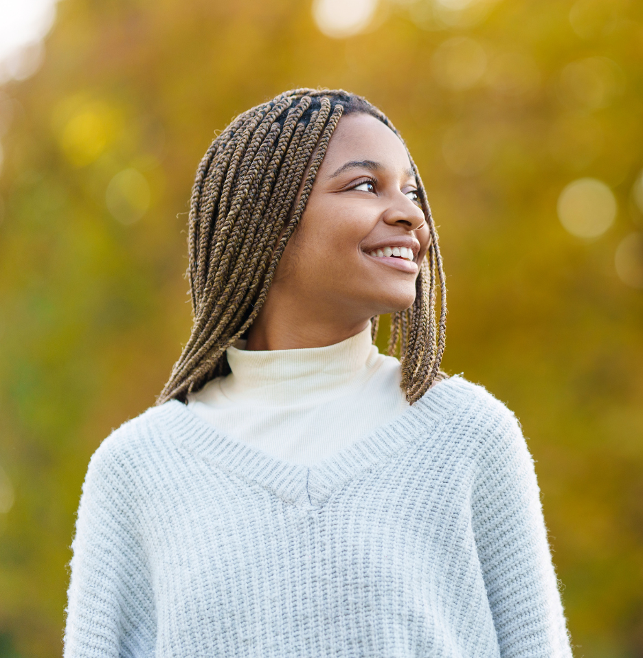 A woman with braids is wearing a blue sweater and smiling.