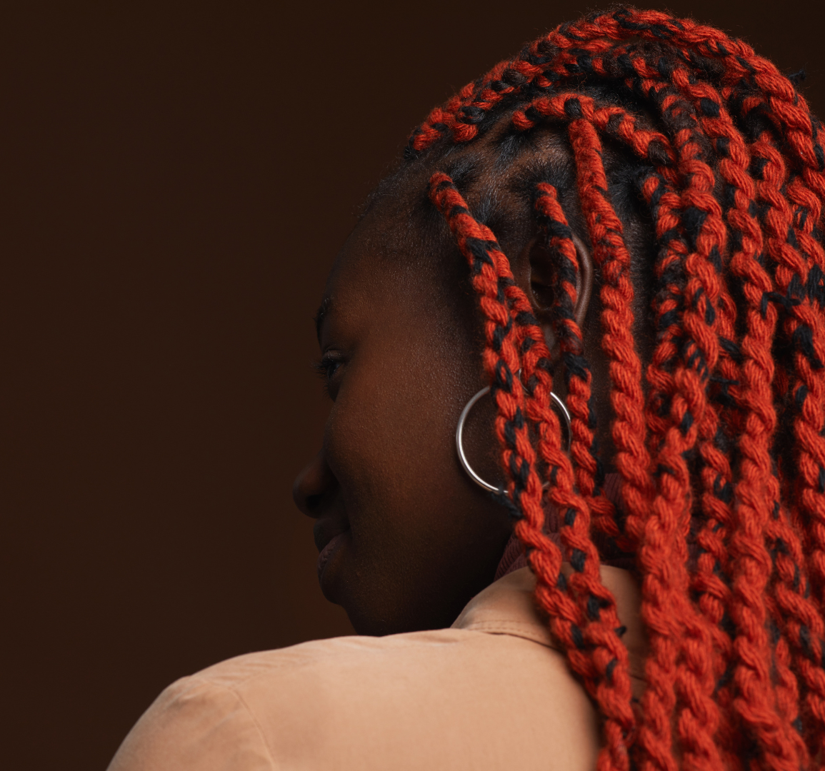 A woman with red braids and earrings is looking over her shoulder.