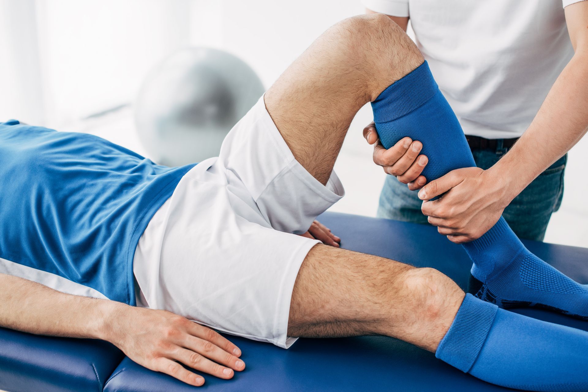 Person receiving physical therapy on their leg; a medical professional holds and moves the patient's leg while they lie on a medical bed.