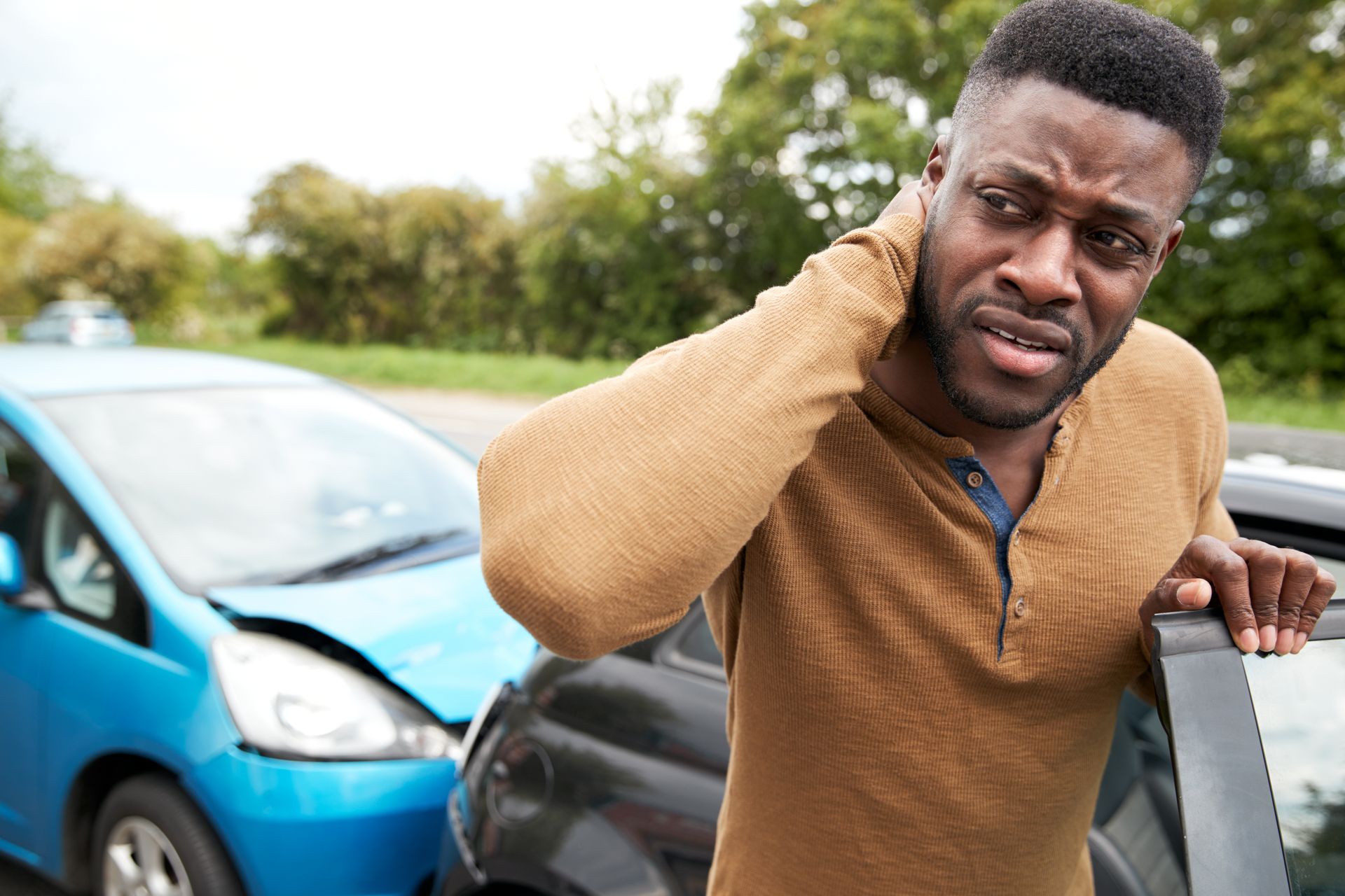 Man holding neck in pain next to damaged cars, likely after a car accident on a road.