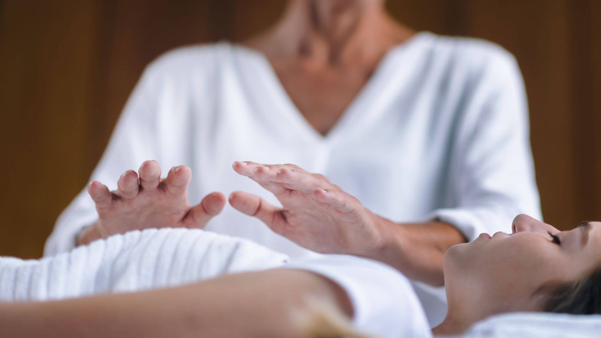 Person receiving Reiki with hands hovering over them, indoors. Another person is performing the Reiki.