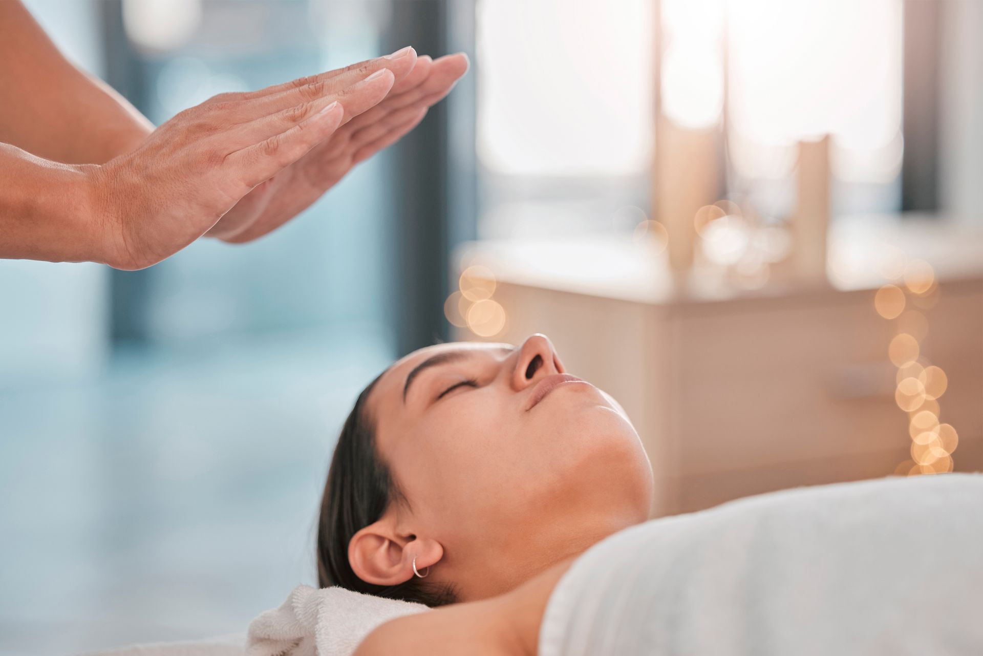 A person receiving a reiki treatment. A practitioner's hands are held above the woman's face as she lies relaxed.