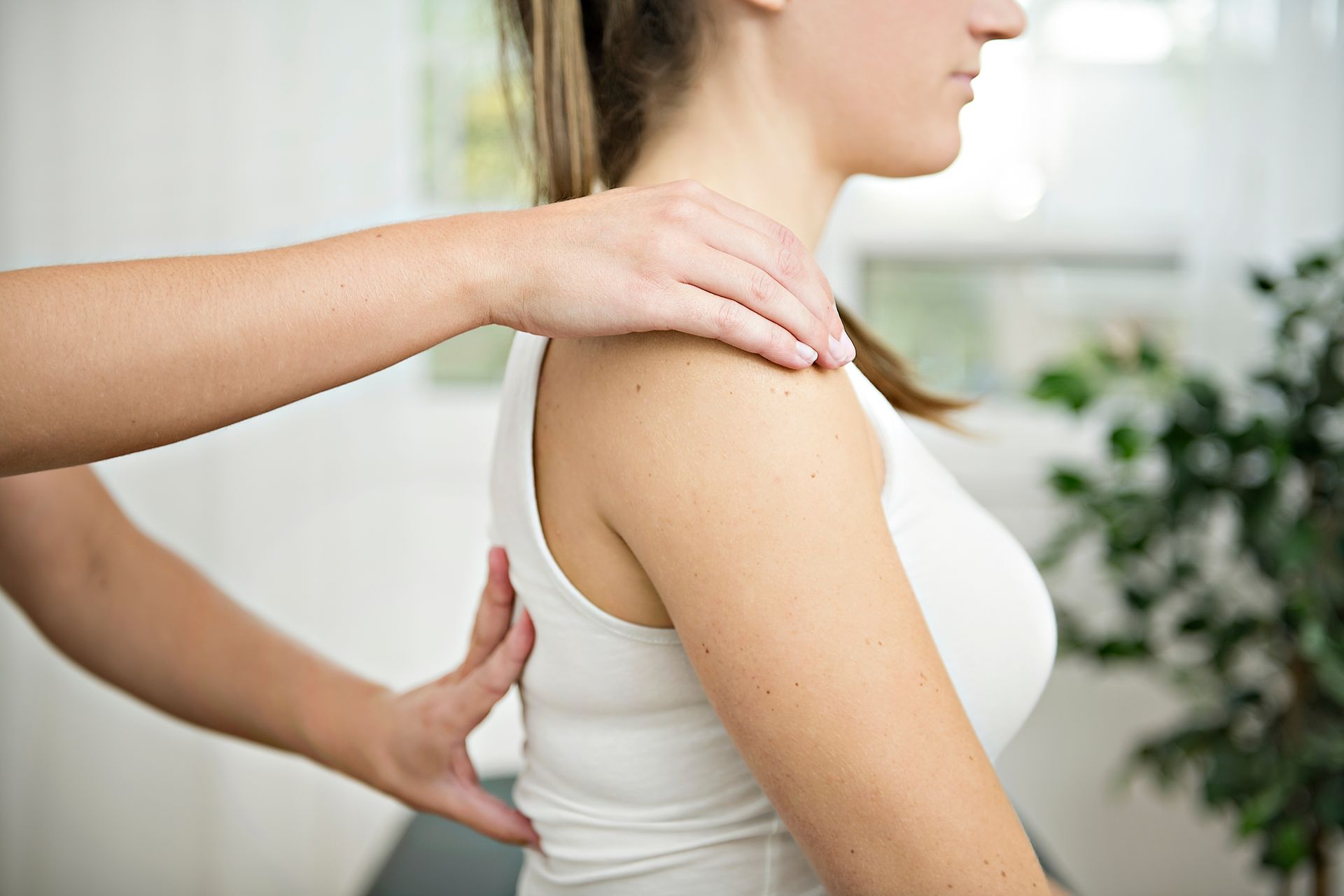Someone's hands are on the shoulders and back of a woman wearing a white tank top.