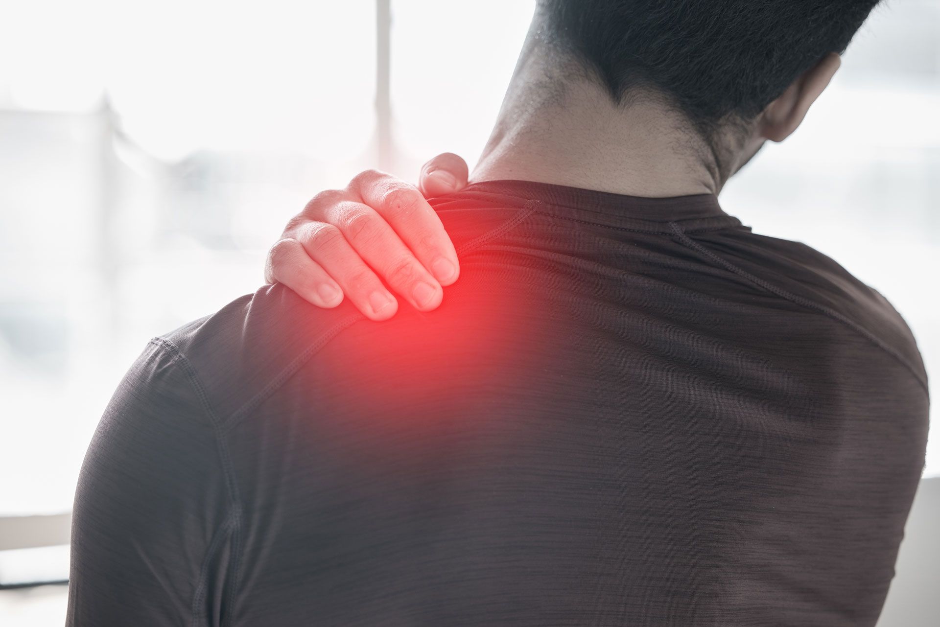 Man holding his shoulder in pain, red highlight indicating injury.