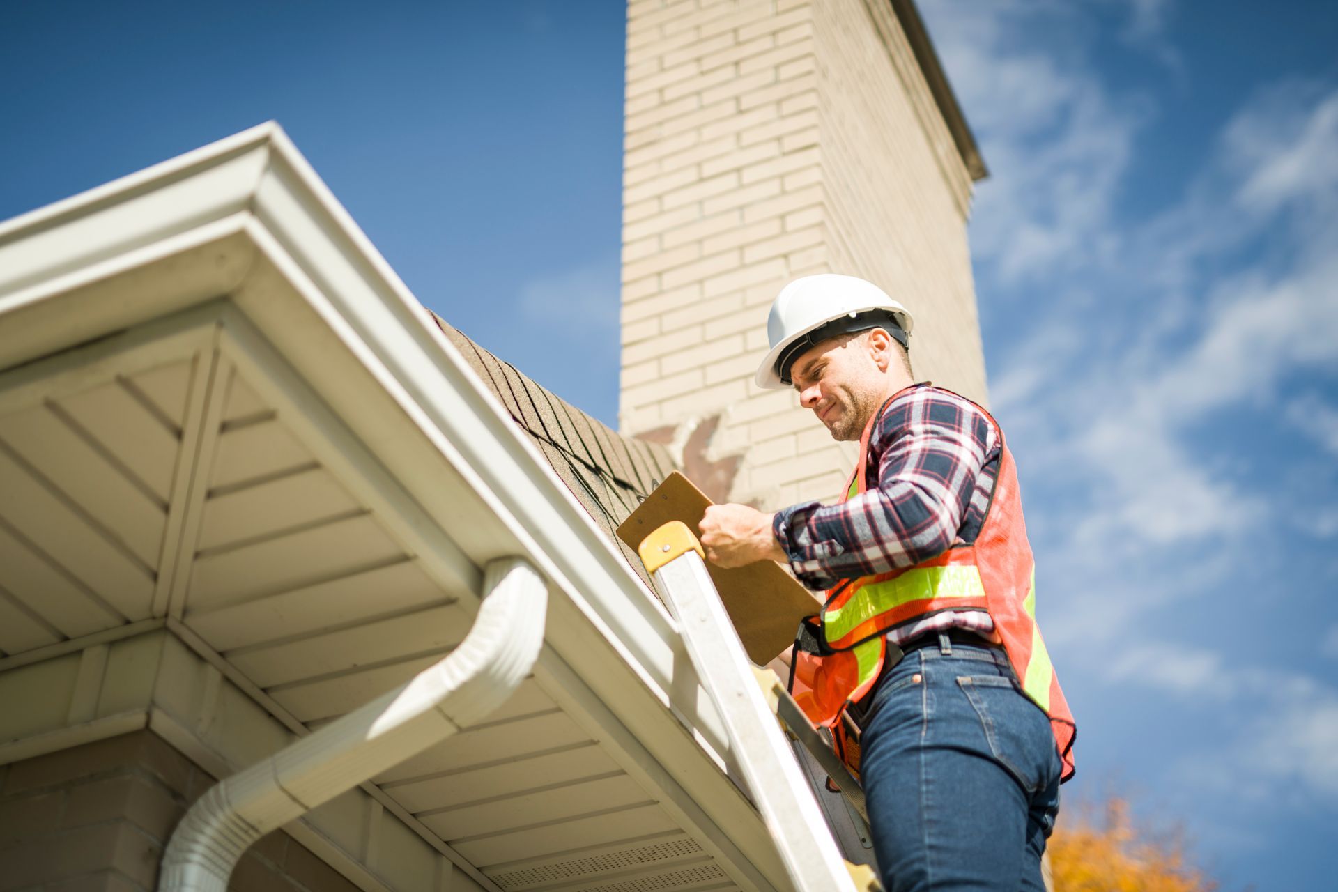 A man is working on a gutter on the roof of a house.