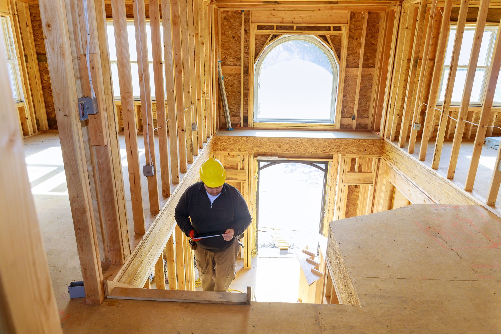 A man in a hard hat is standing in a wooden house under construction.