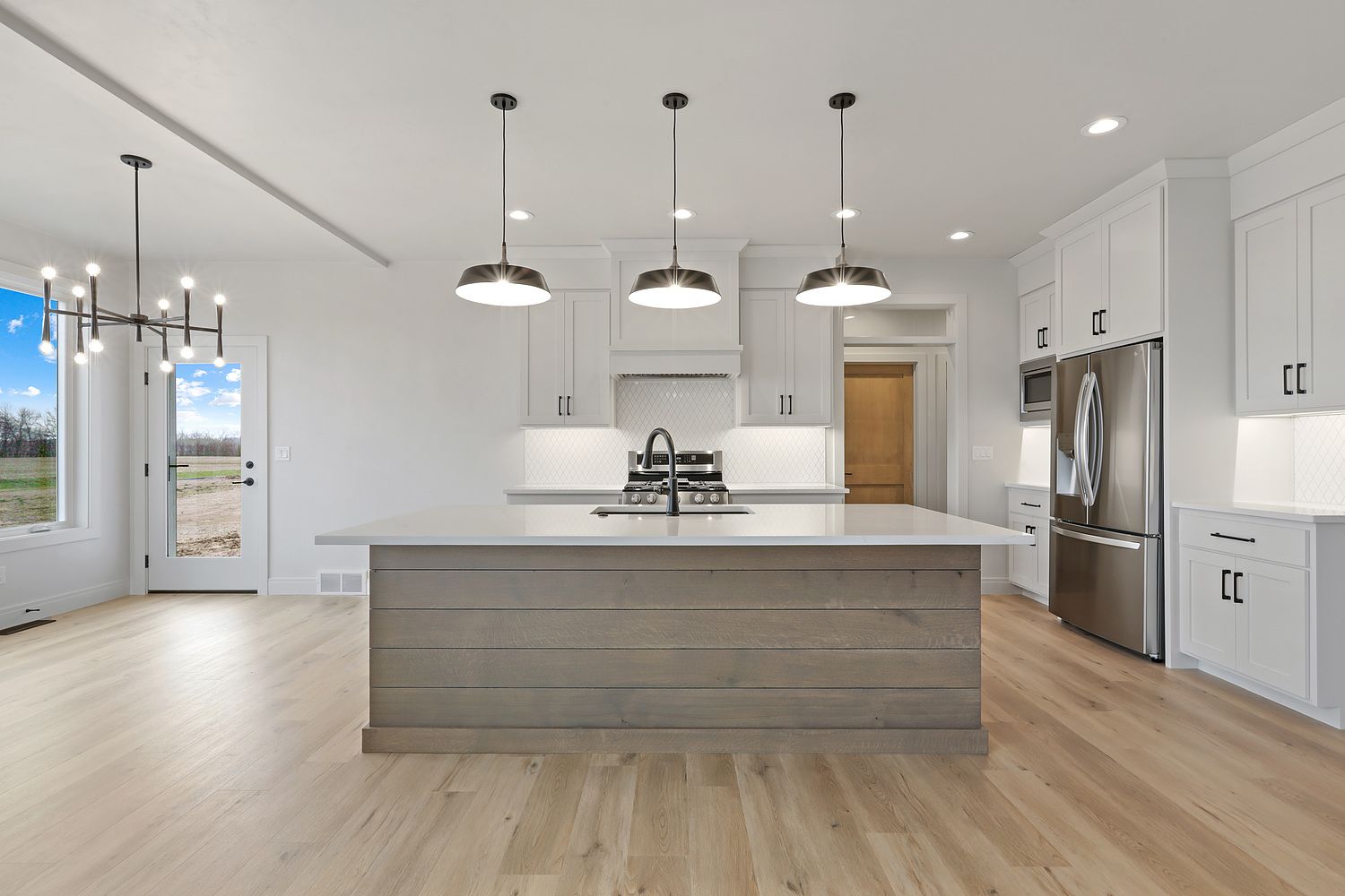 Modern white kitchen with a large island, stainless steel appliances, and light wood flooring.