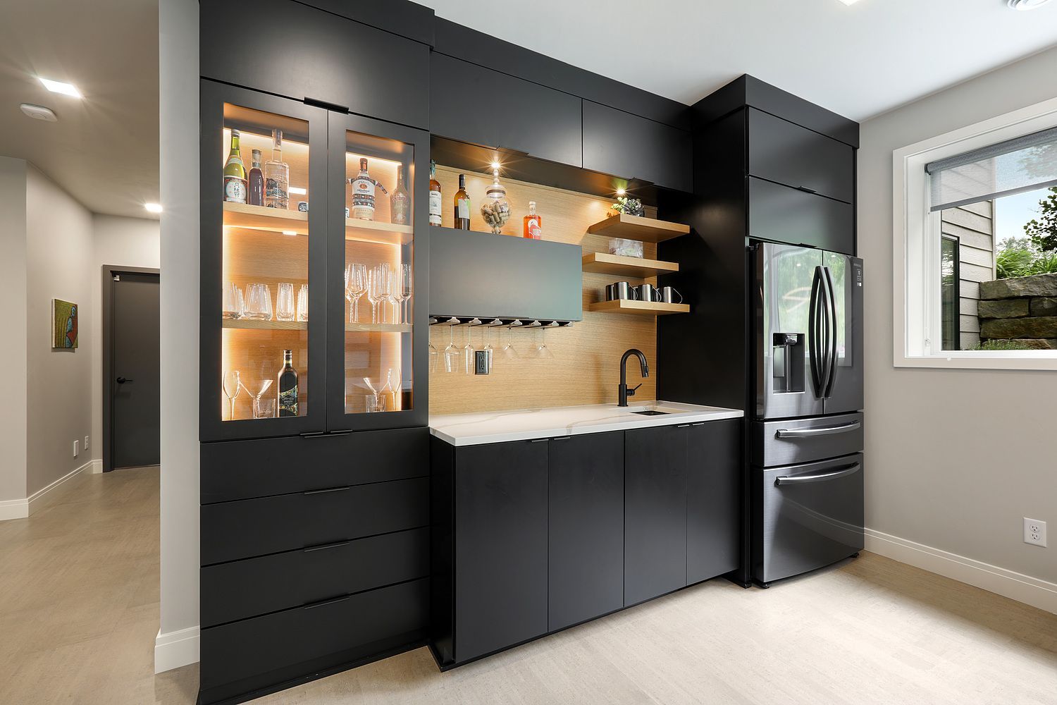 A kitchen with black cabinets , a refrigerator , a sink and a window.
