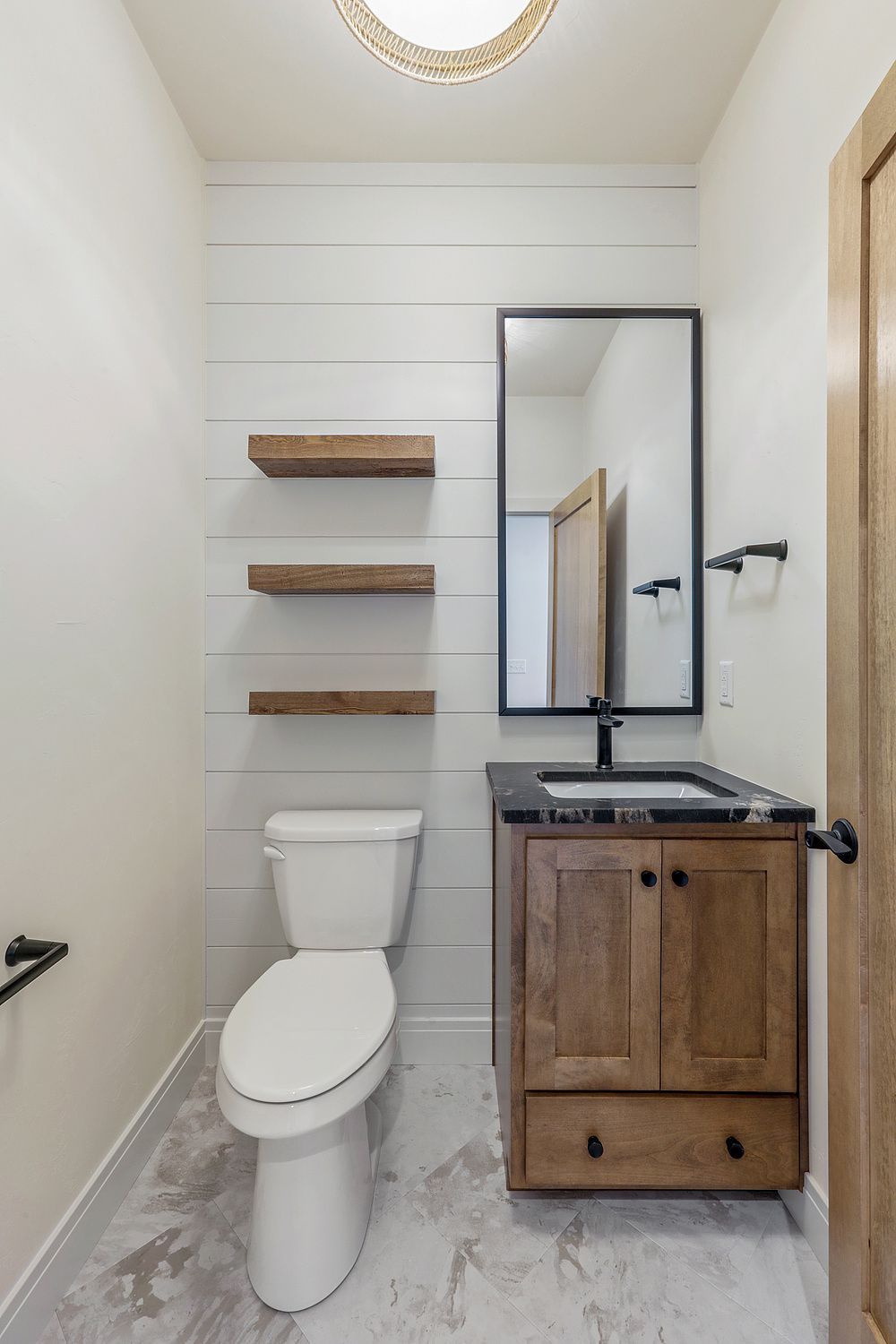 A bathroom with a toilet , sink , mirror and shelves.