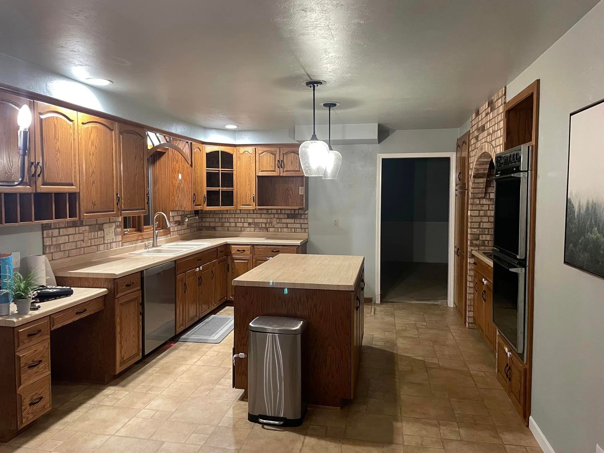 A kitchen with wooden cabinets , stainless steel appliances , a large island and a trash can.