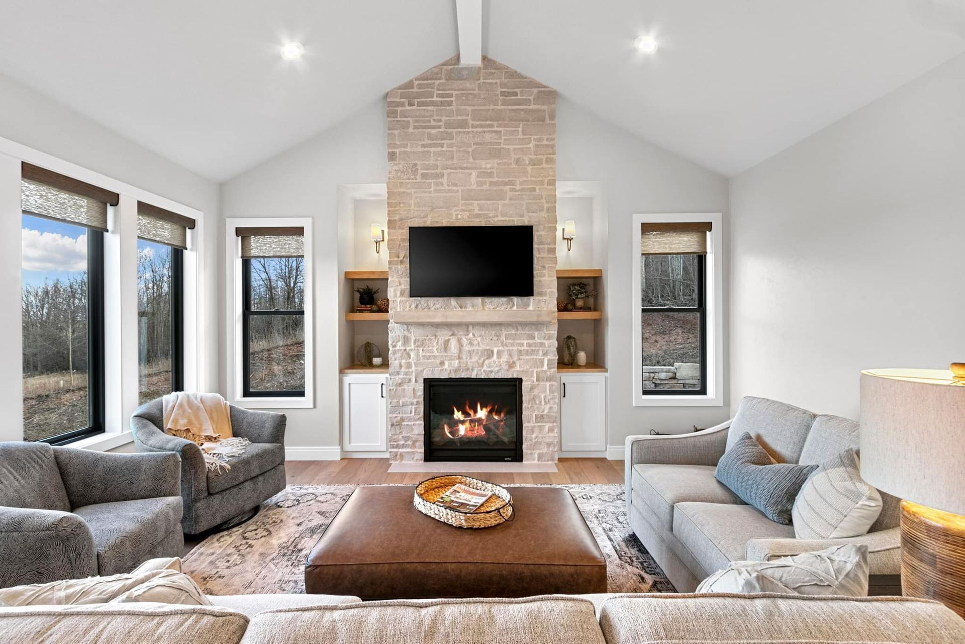 Living room with fireplace, grey furniture, large windows, and neutral tones.