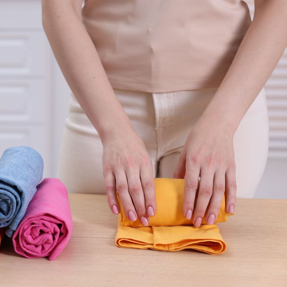 A woman is folding a yellow towel on a wooden table.