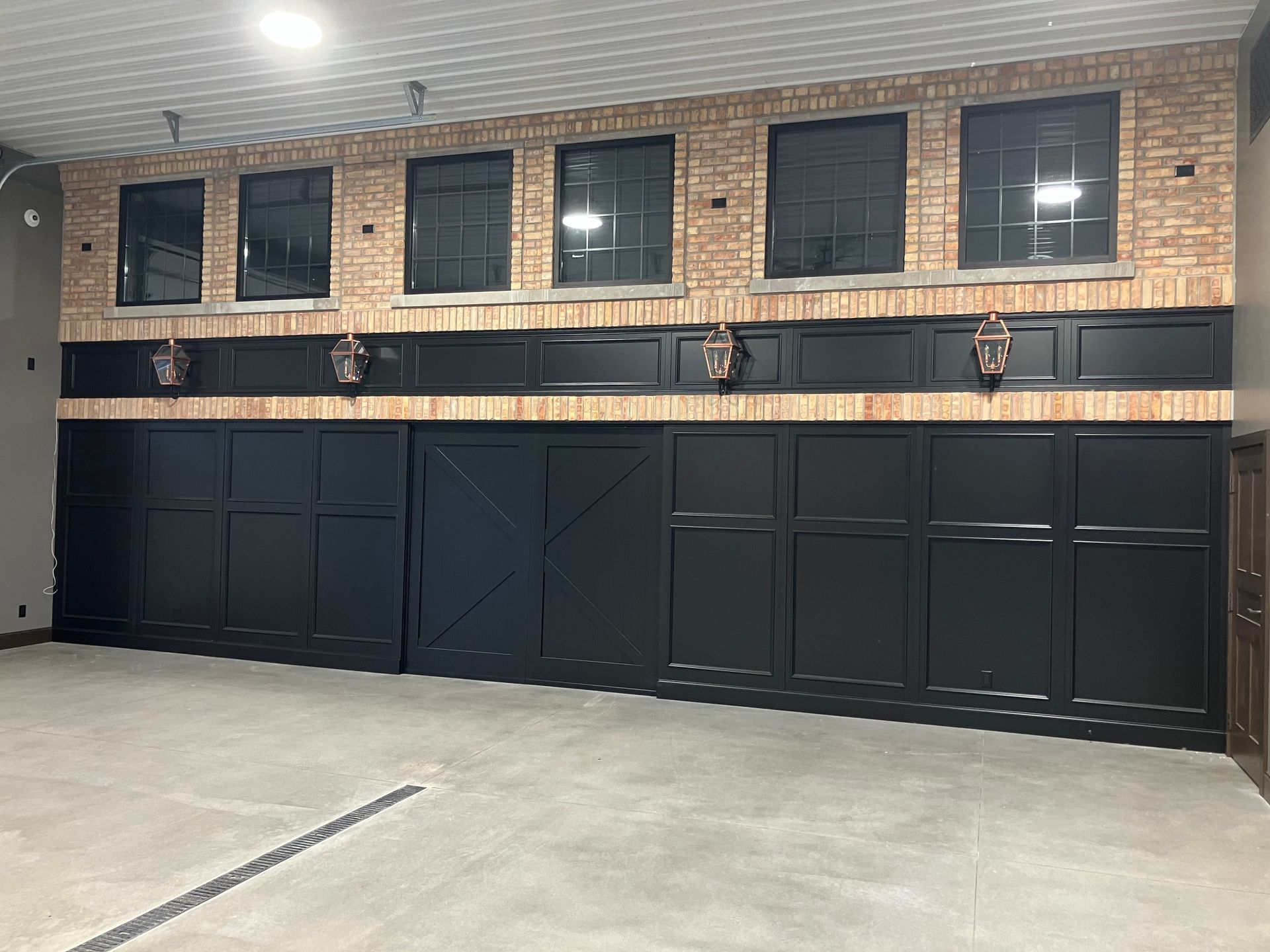 Black paneled wall with brick accents, windows, and animal heads in a large, empty room.