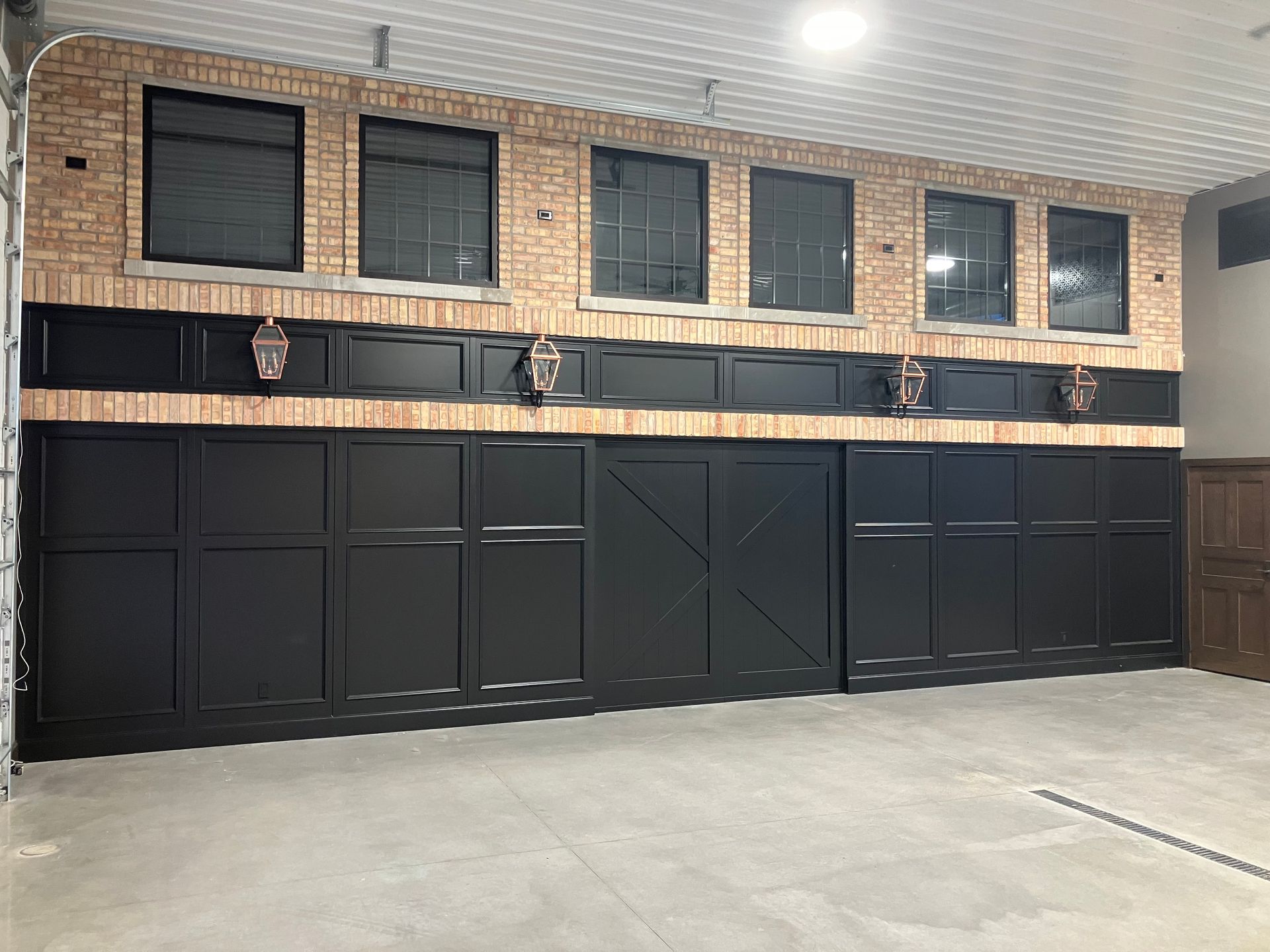 Black paneling and brick wall in a garage. Windows across the top, falcon decor, a barn door.