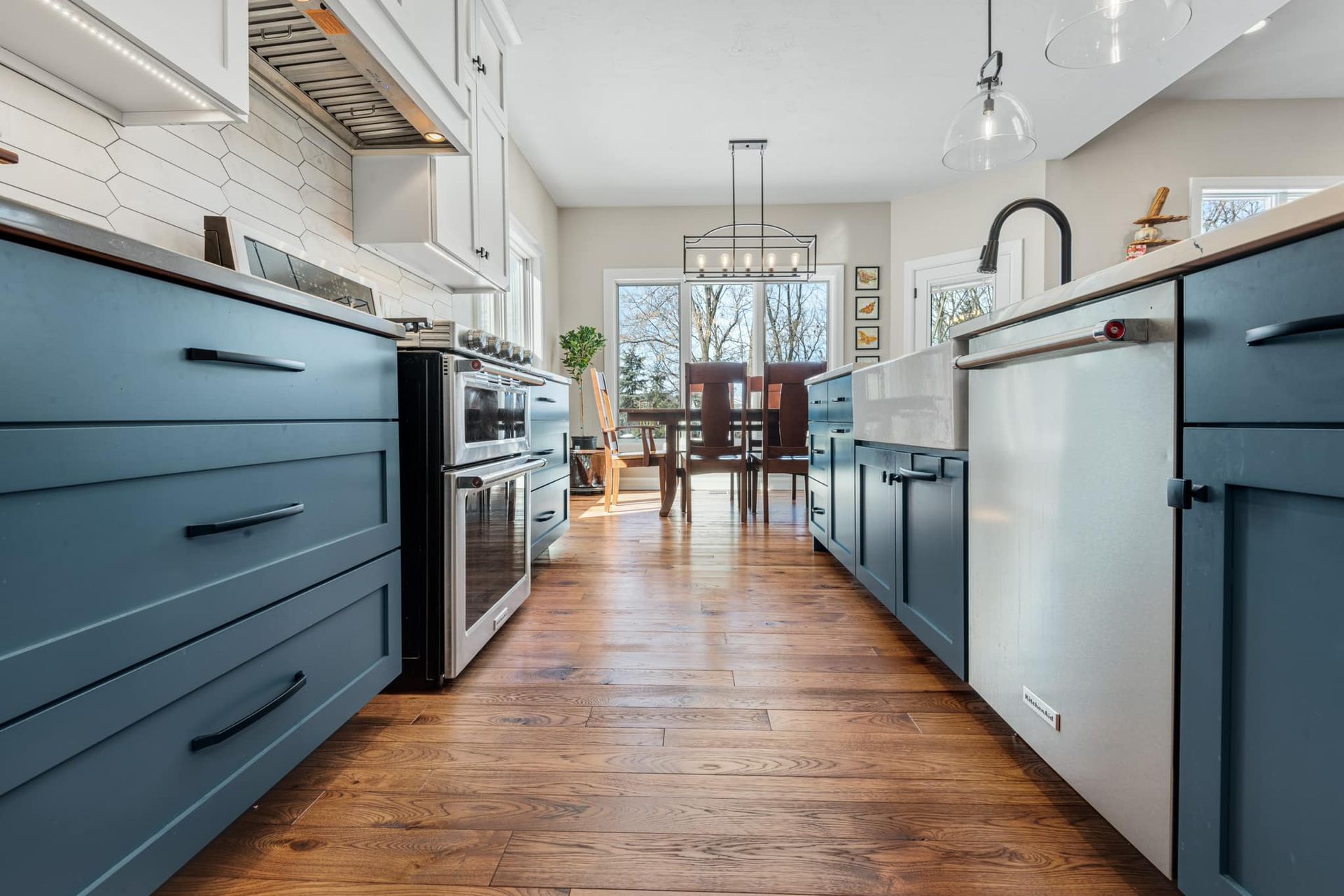 A kitchen with blue cabinets , white cabinets , stainless steel appliances and hardwood floors.
