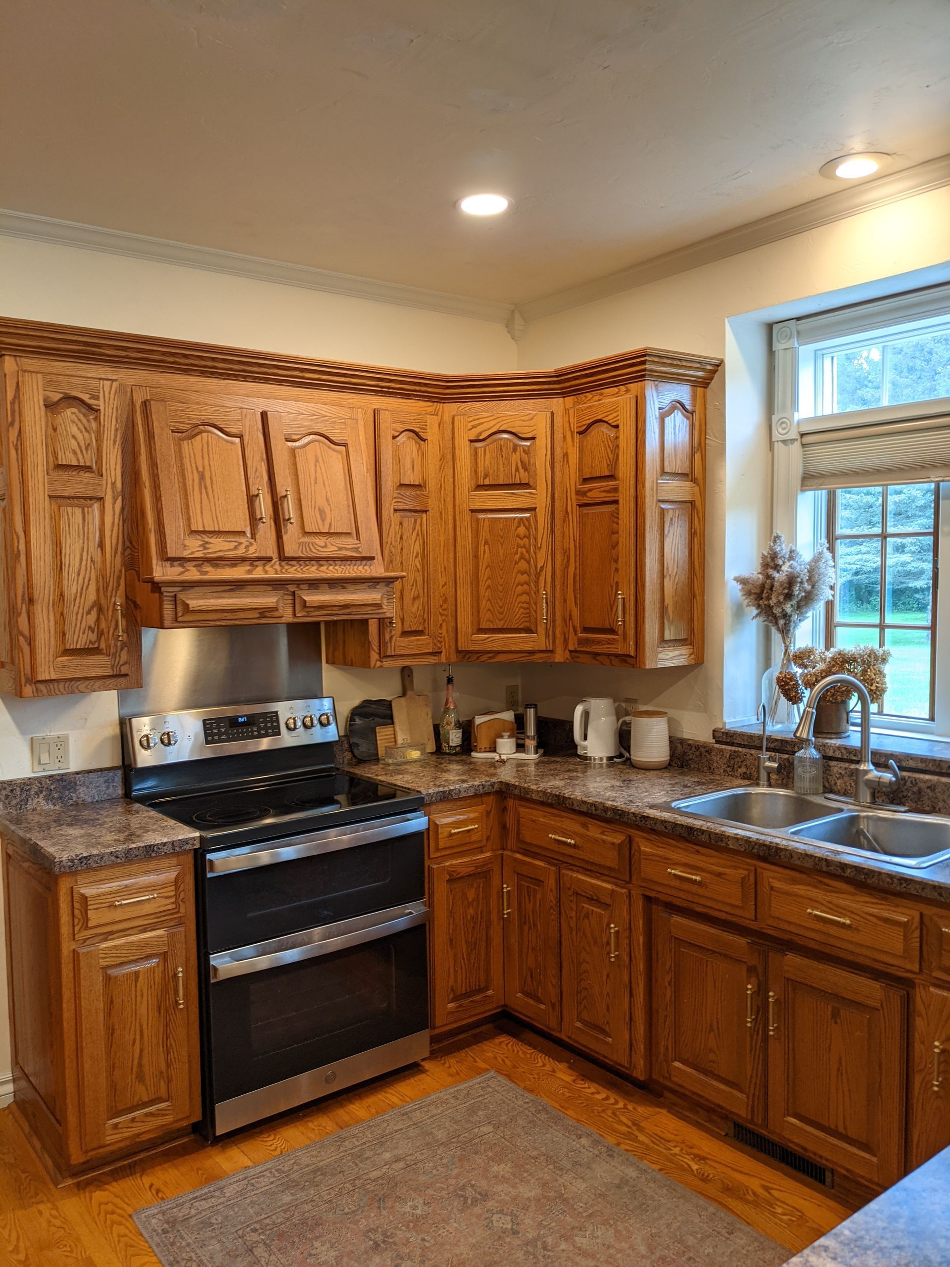 Kitchen with wooden cabinets, stainless steel appliances, and a window overlooking greenery.