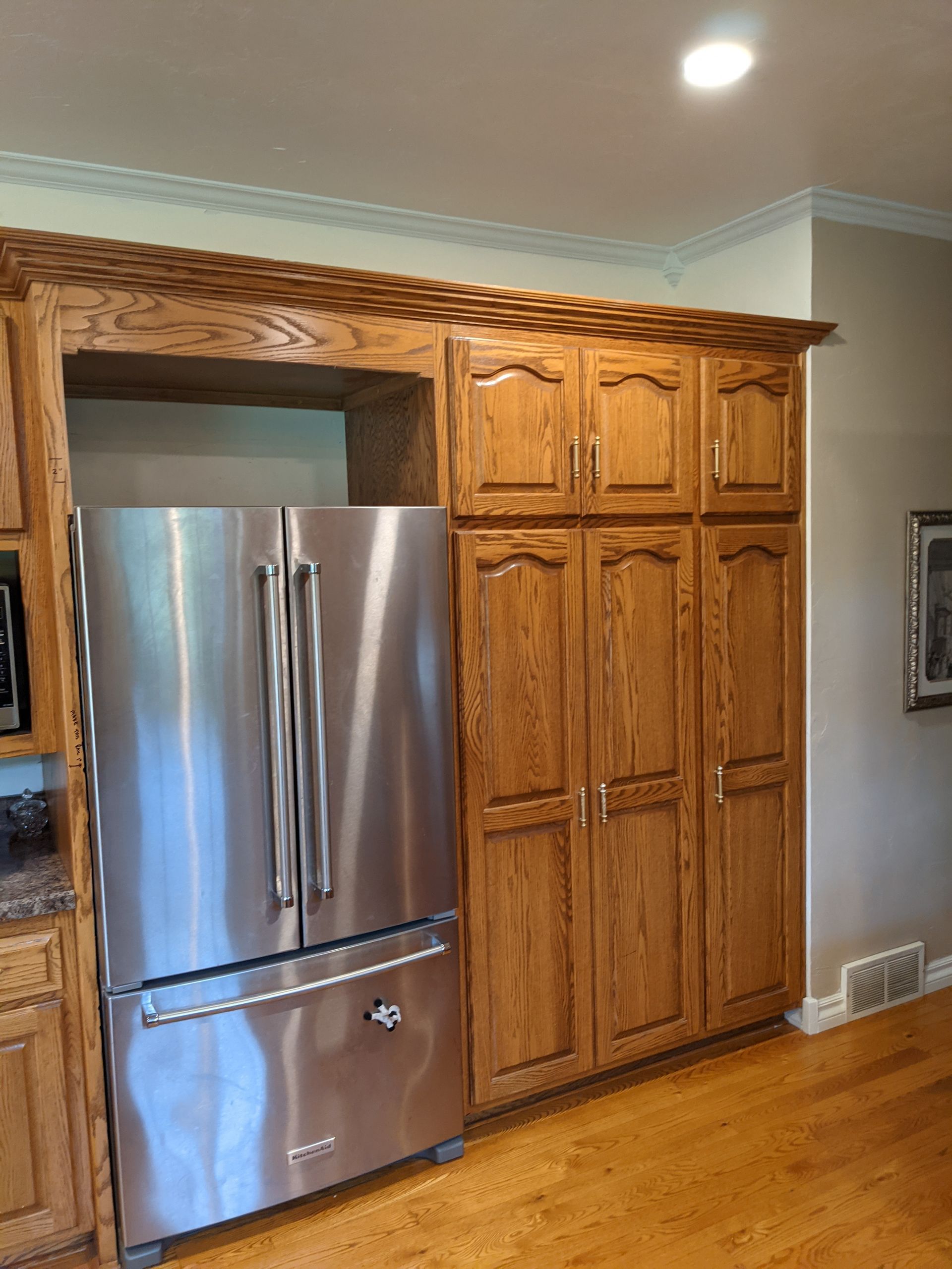 Refrigerator, cabinets, and pantry in a kitchen with wood flooring and trim. Stainless steel fridge.