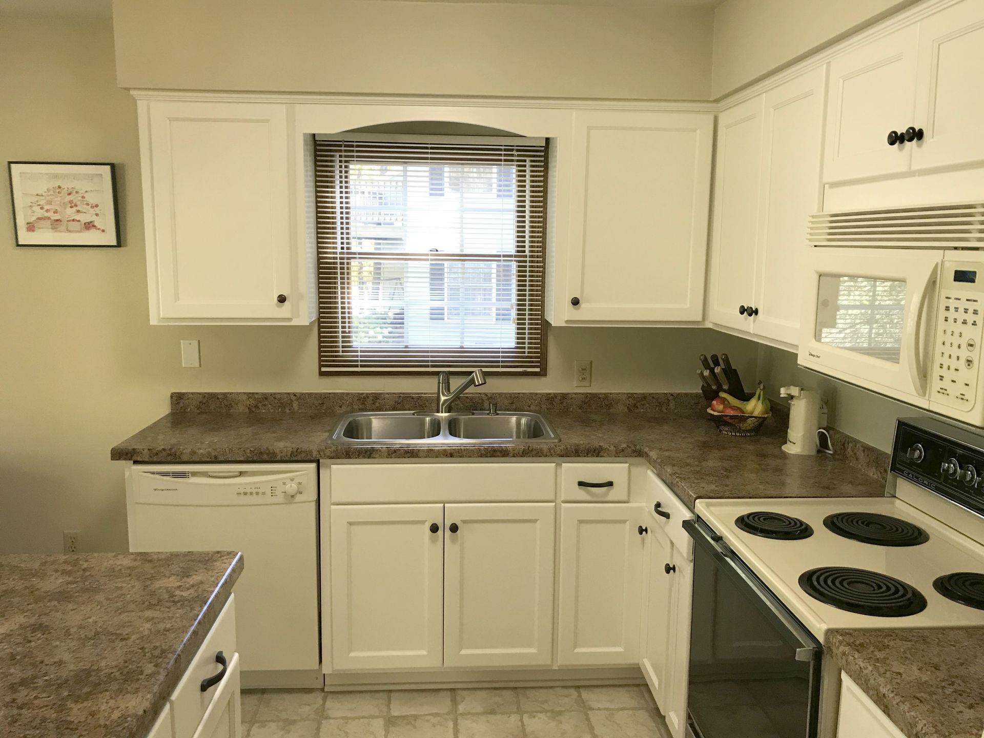 A kitchen with white cabinets , a stove , a sink , and a window.