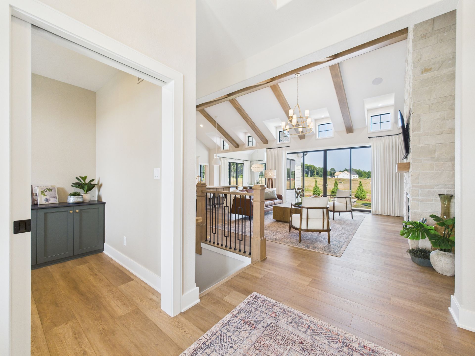 A modern home interior with vaulted ceilings, wooden beams, and large windows overlooking a green landscape.