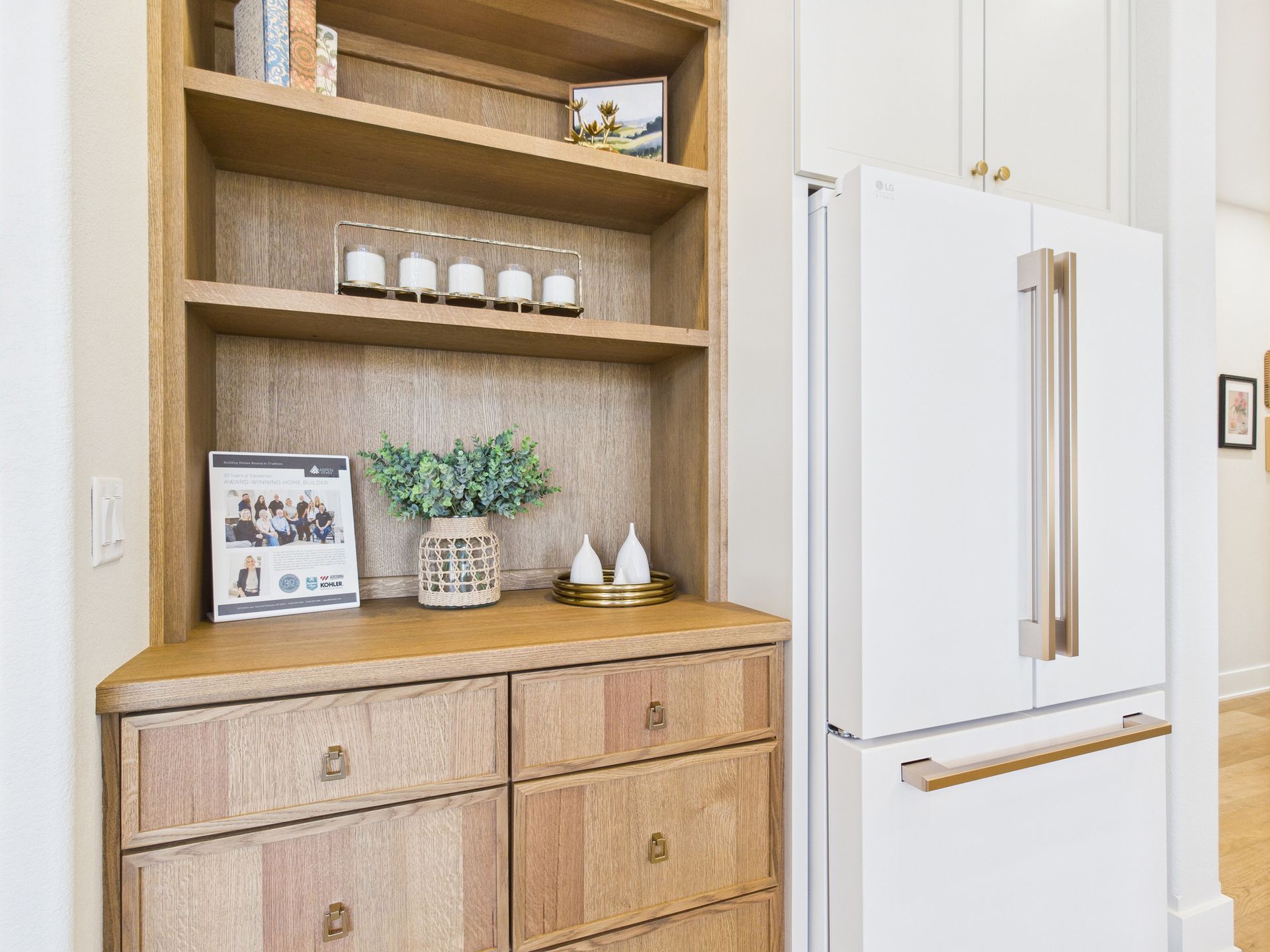 Wooden built-in cabinet with shelves, drawers, and decor next to a white refrigerator in a kitchen.