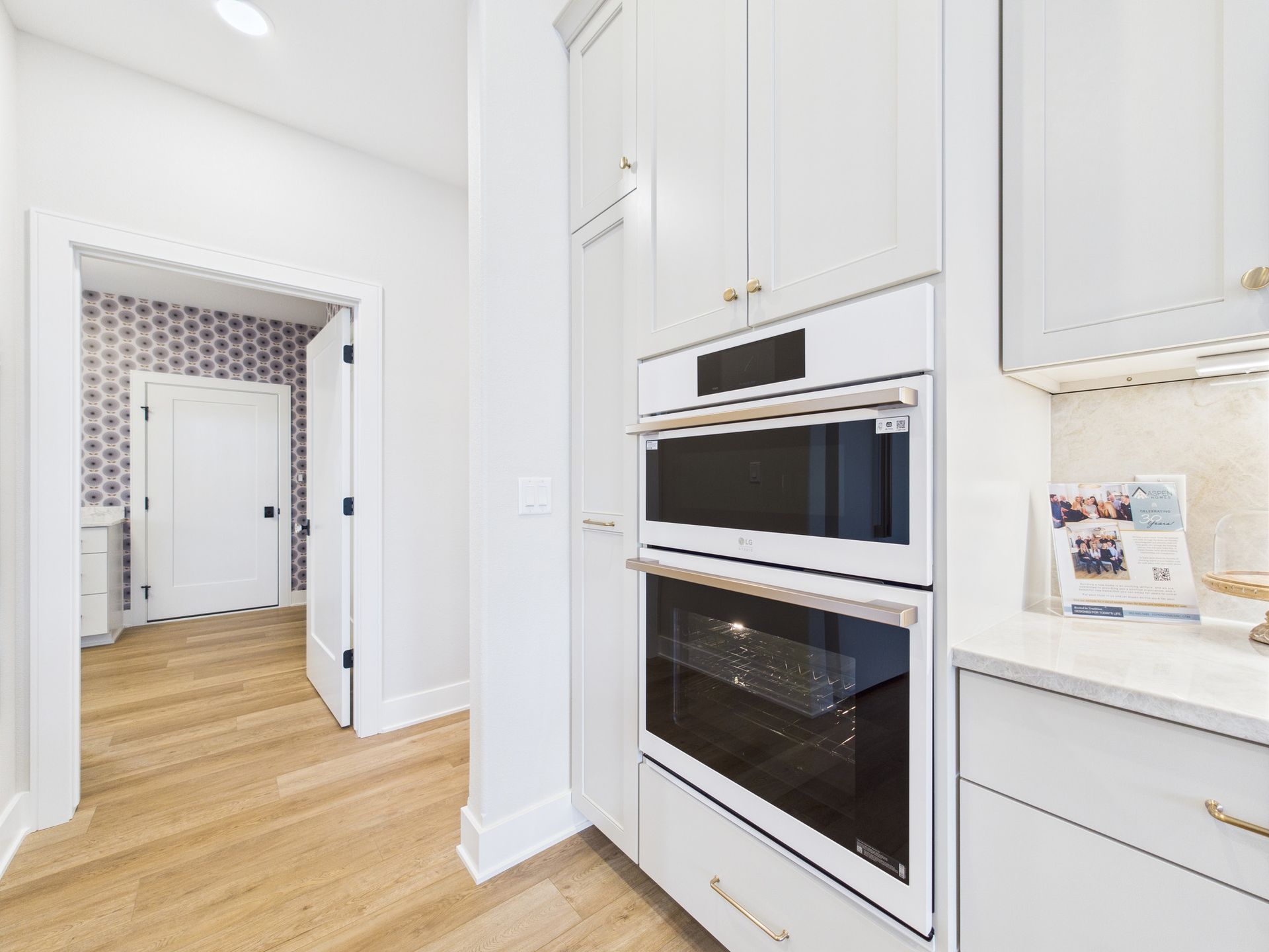 White kitchen cabinets with a built-in oven and microwave. An open door leads to a laundry room.