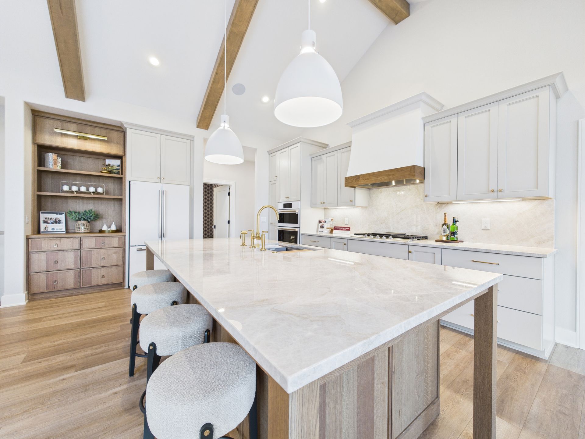 Bright kitchen with light cabinetry, marble island, wooden beams, and stools.