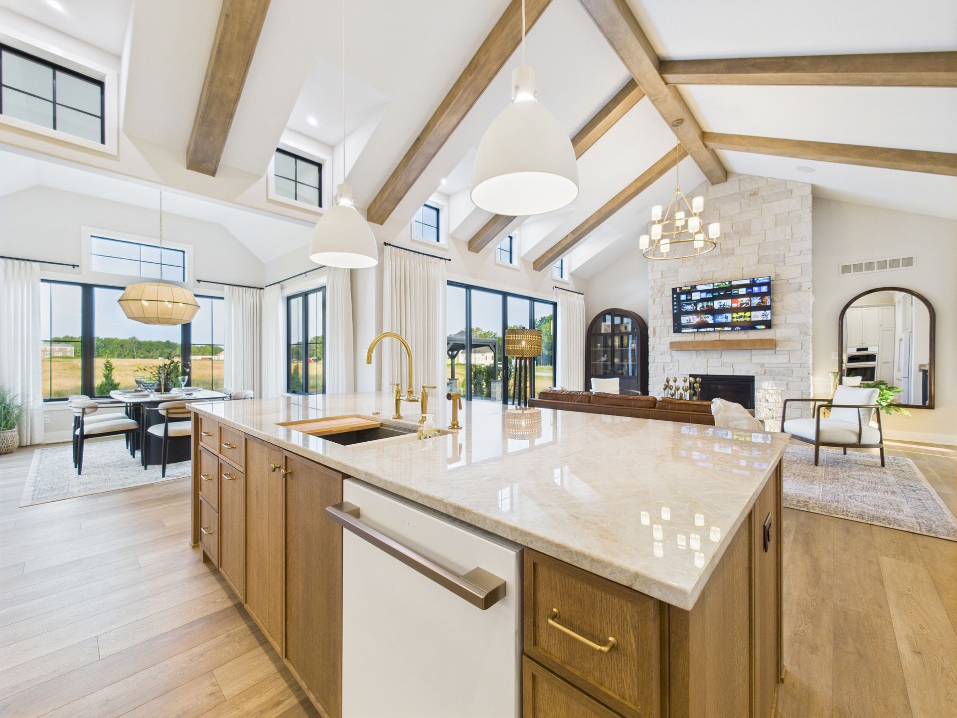 Spacious kitchen with wooden cabinets, large island, and vaulted ceiling with exposed beams; opens to dining and living areas.