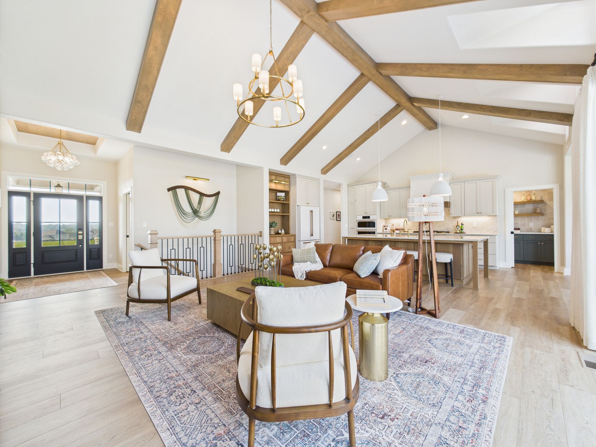 Spacious living room with vaulted ceiling, exposed beams, leather sofa, armchairs, and open kitchen.