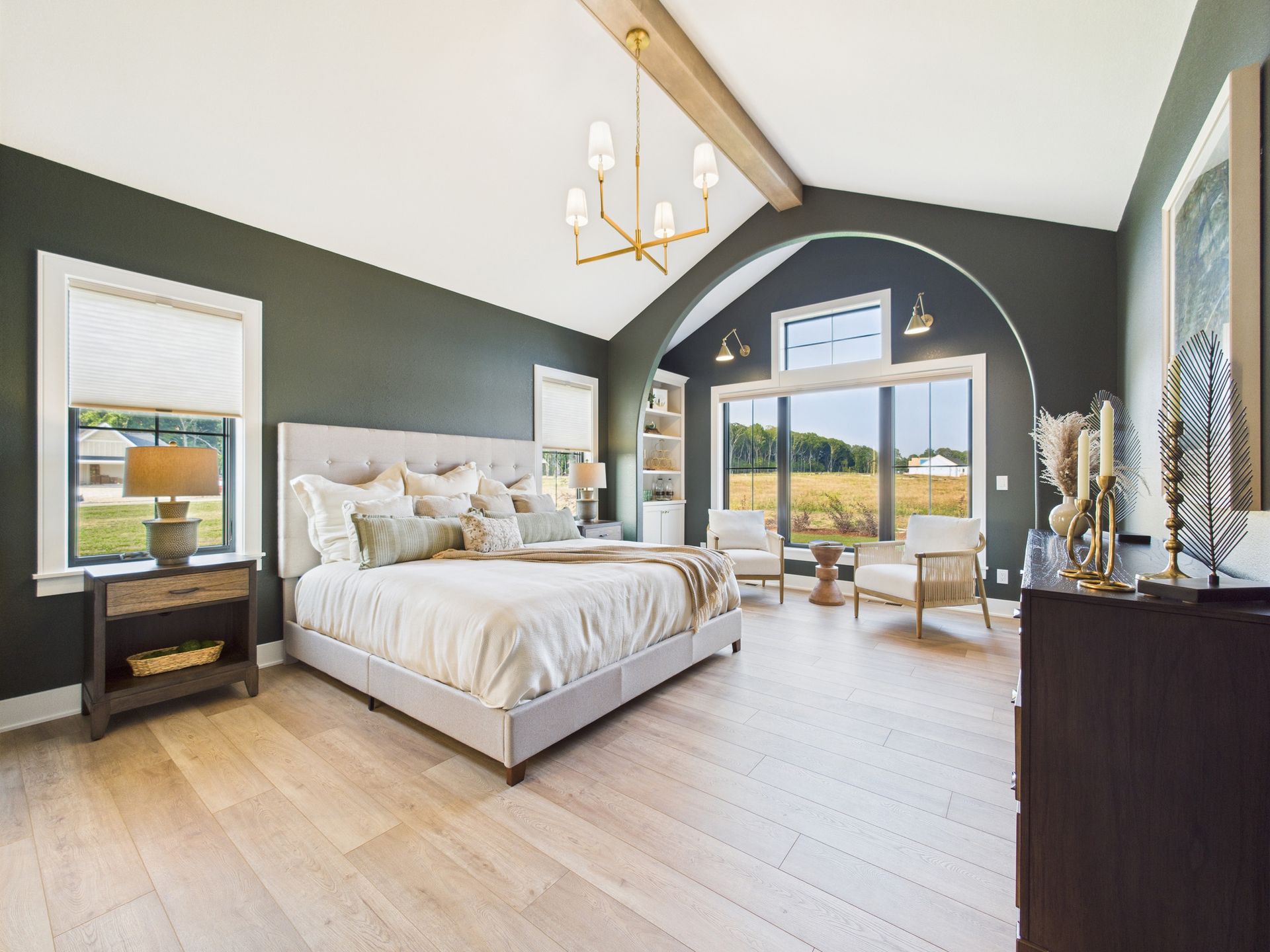 Spacious master bedroom with a king-sized bed, dark green walls, and a large window overlooking a field.