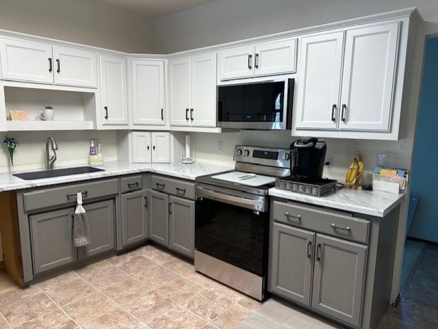 A kitchen with gray cabinets , stainless steel appliances , a stove , microwave and sink.