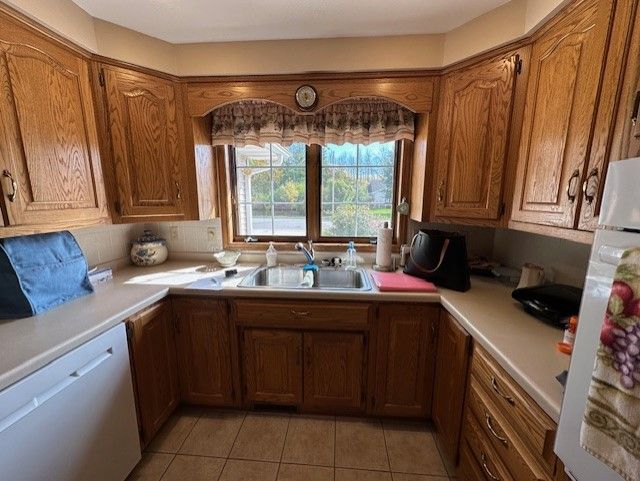 A kitchen with wooden cabinets , a sink , a refrigerator , and a window.