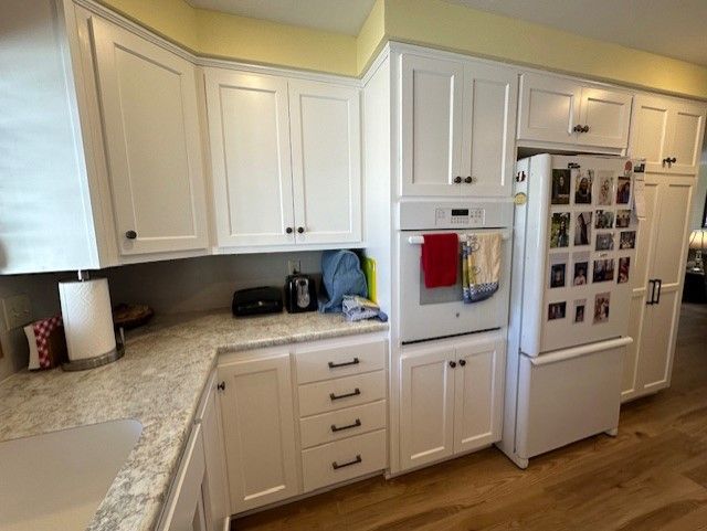 A kitchen with white cabinets , a refrigerator , and a sink.