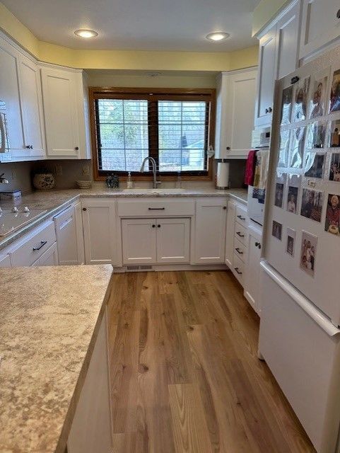 A kitchen with white cabinets , hardwood floors , a refrigerator and a sink.
