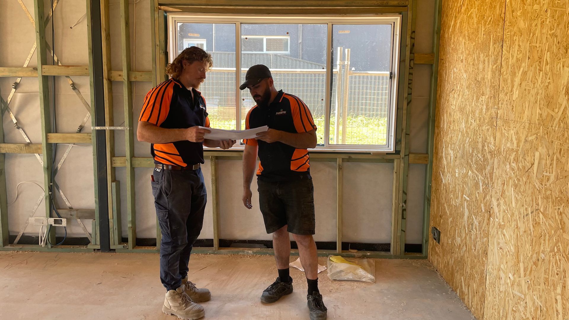 Two men are standing in a room looking at a piece of paper.