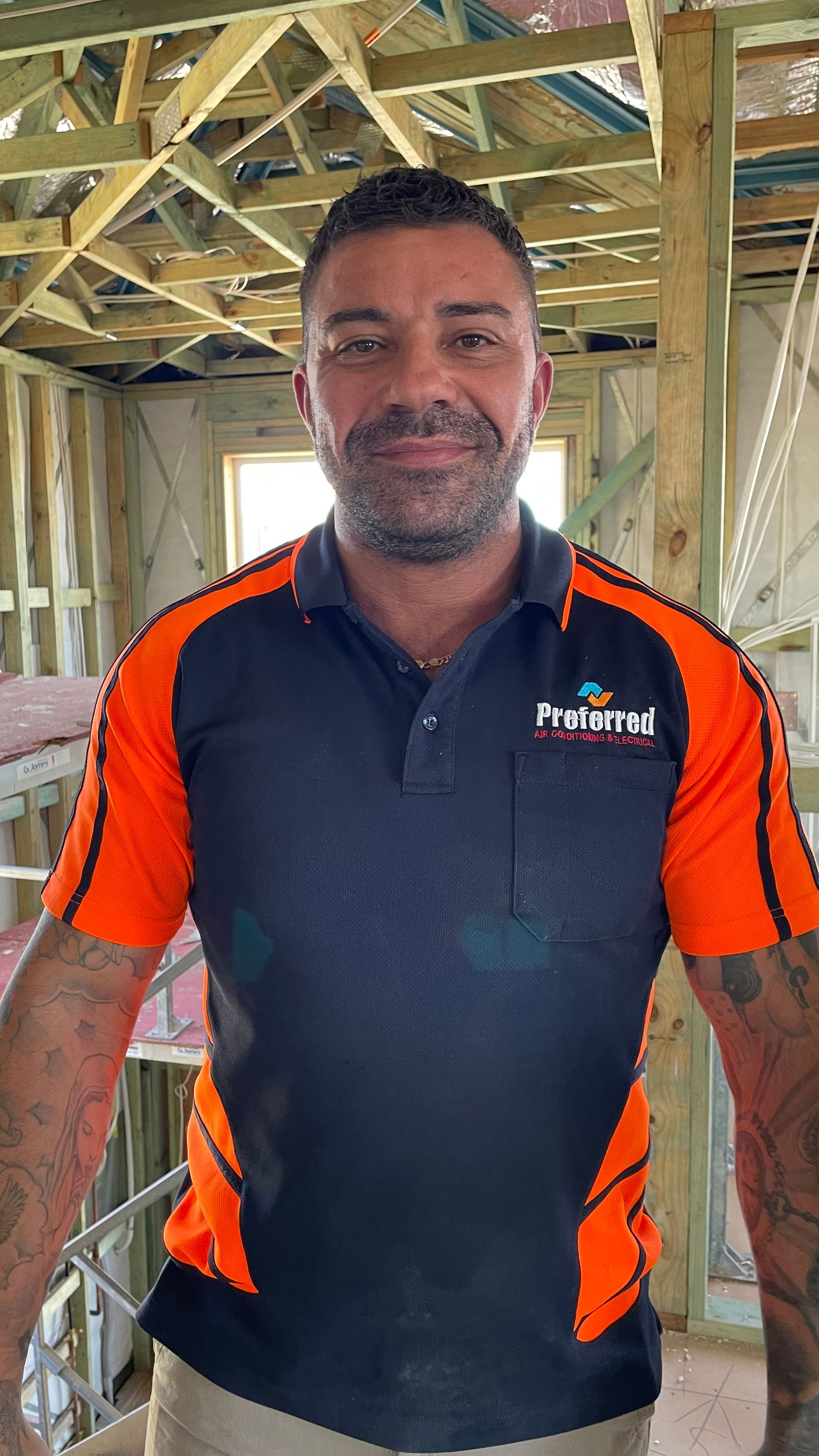 A man in an orange and black shirt is standing in a building under construction.